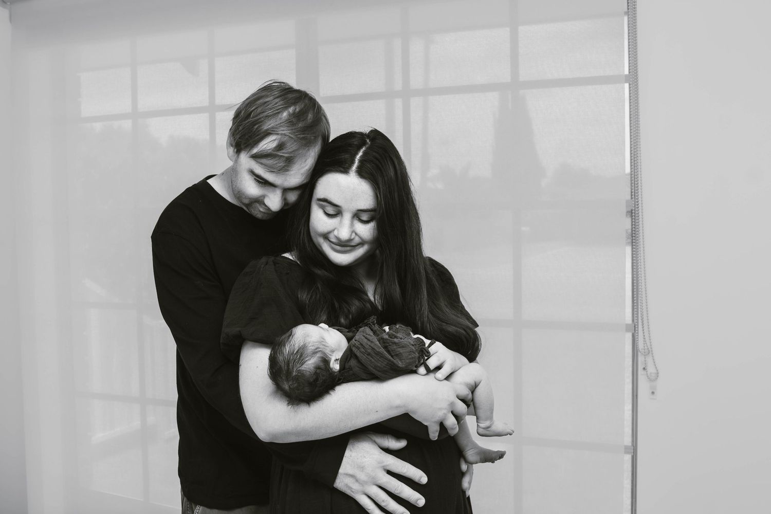 A black and white photo captures new parents sharing tender moments with their infant.
