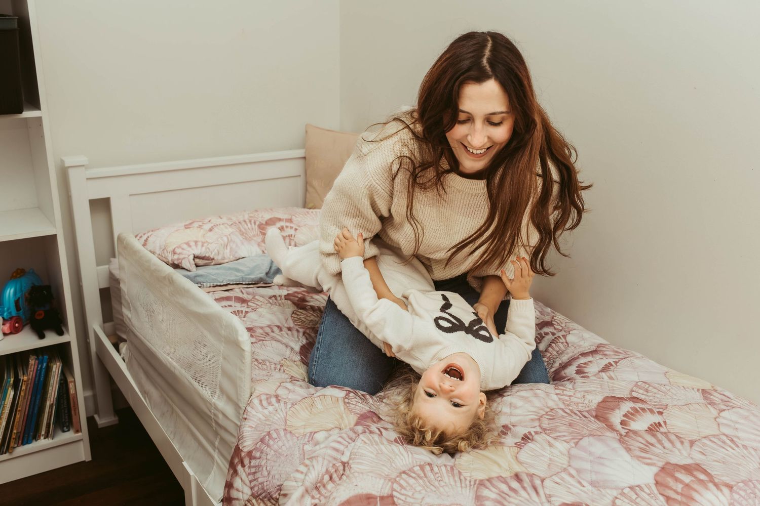 mother tickles toddler girl on bed