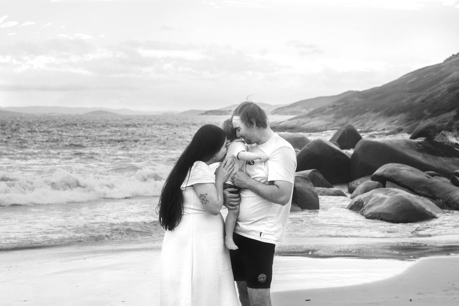 Black and white image of a family sharing an intimate moment on a coastal beach.