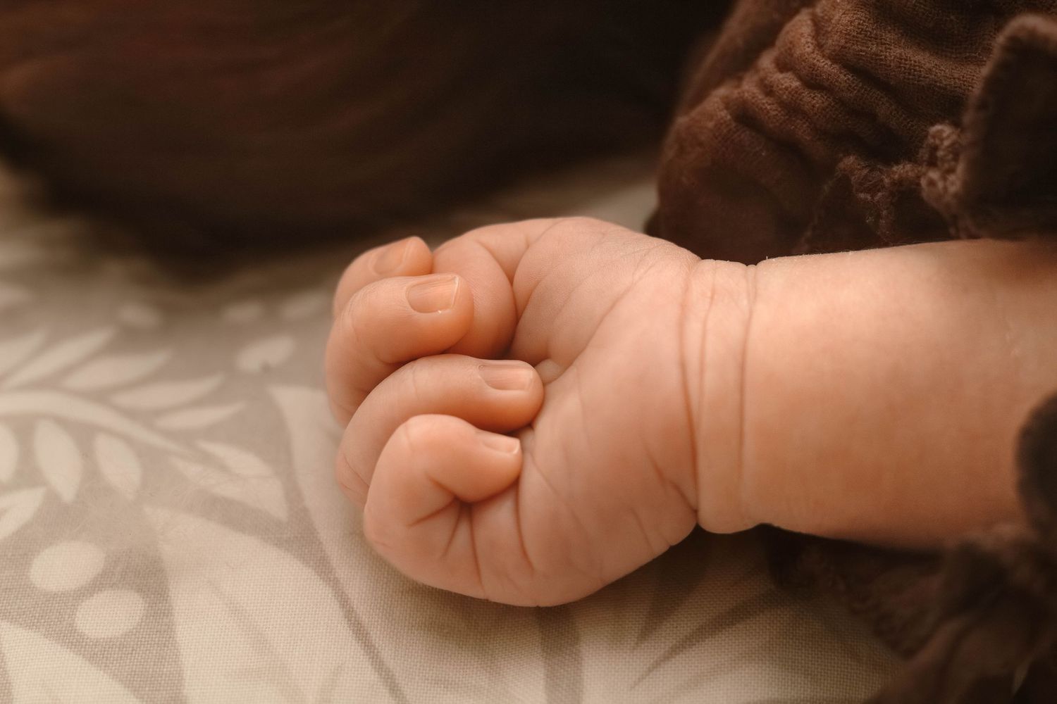 Close-up view of a tiny baby's hand against a patterned fabric background.