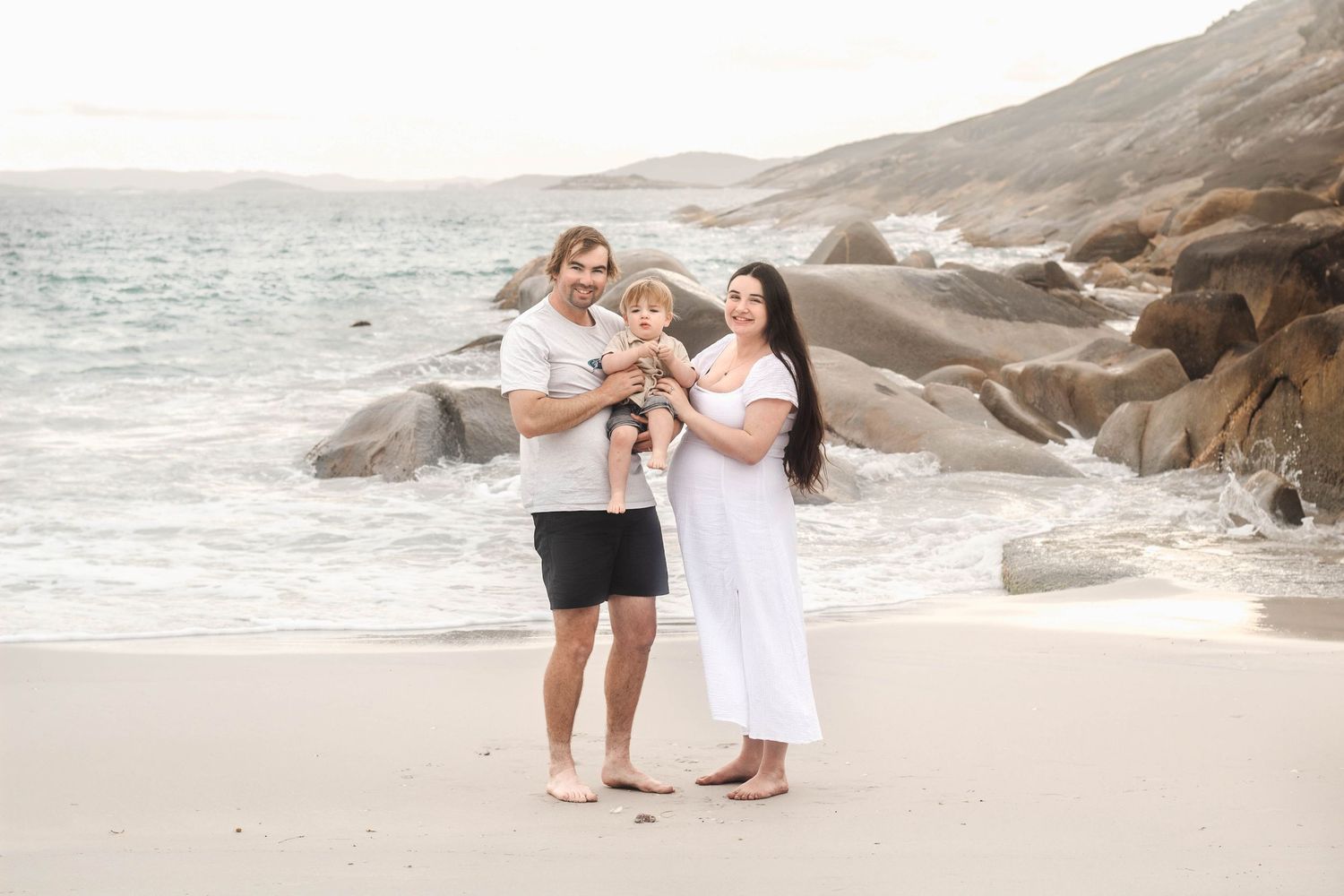 A family of three enjoys quality time together on a scenic beach with large boulders.