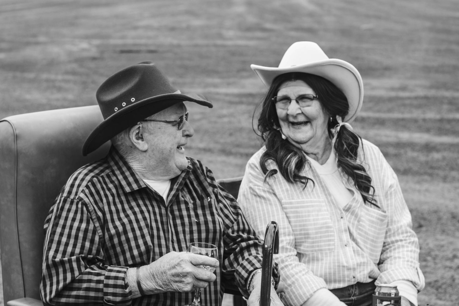 Black and white photo of two people in cowboy hats sharing a hearty laugh outdoors.
