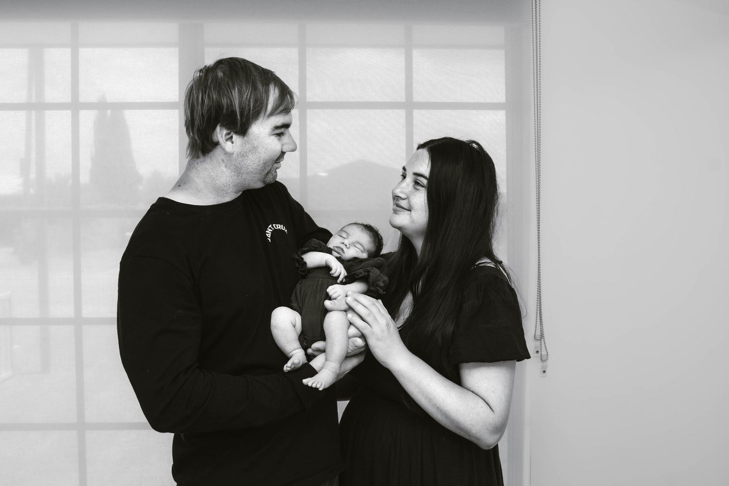 A black and white portrait of new parents sharing a joyful moment with their infant.