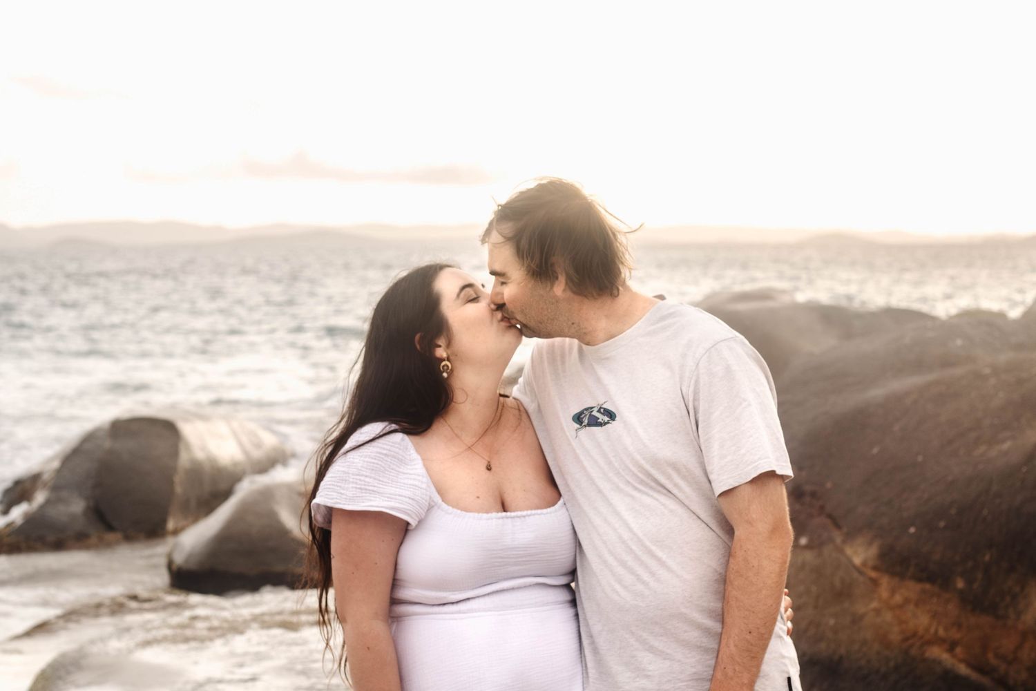Romantic couple sharing an intimate moment on a rocky beach at sunset.