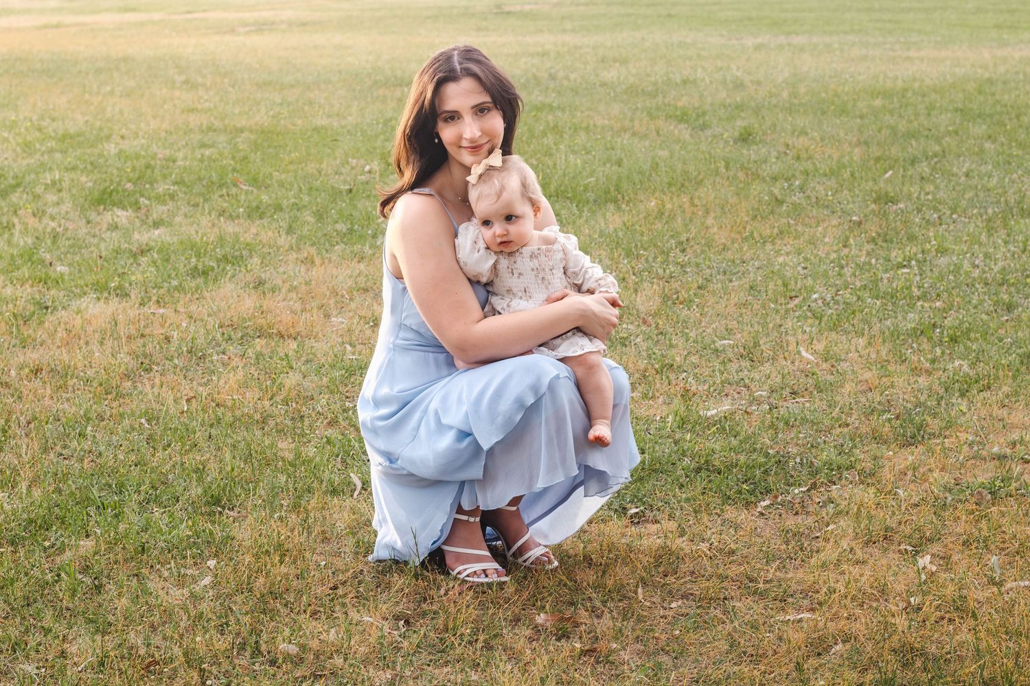 Parent and baby sharing a tender moment together on grassy field.