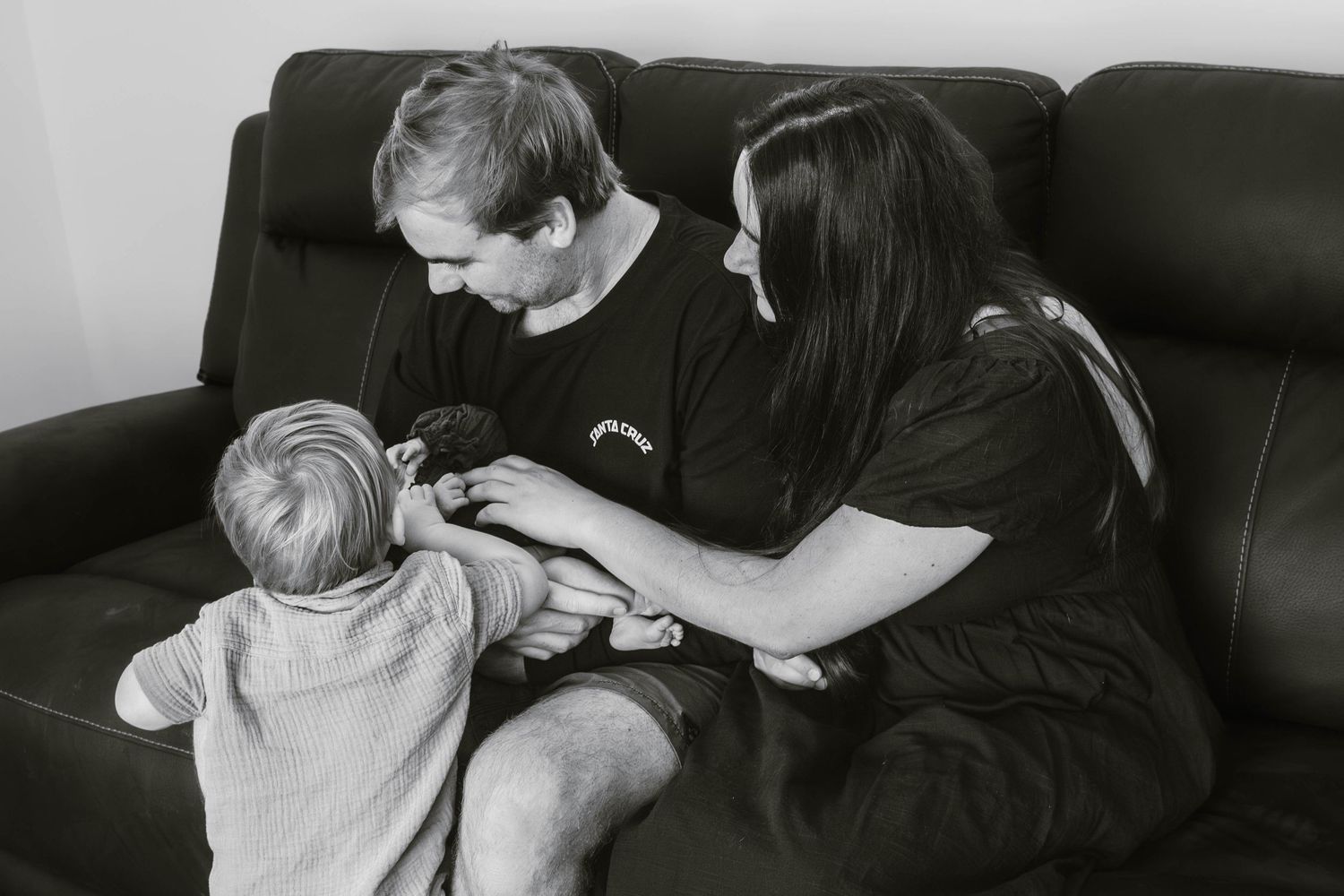 Family sharing intimate moment together on brown leather couch in black and white photograph.