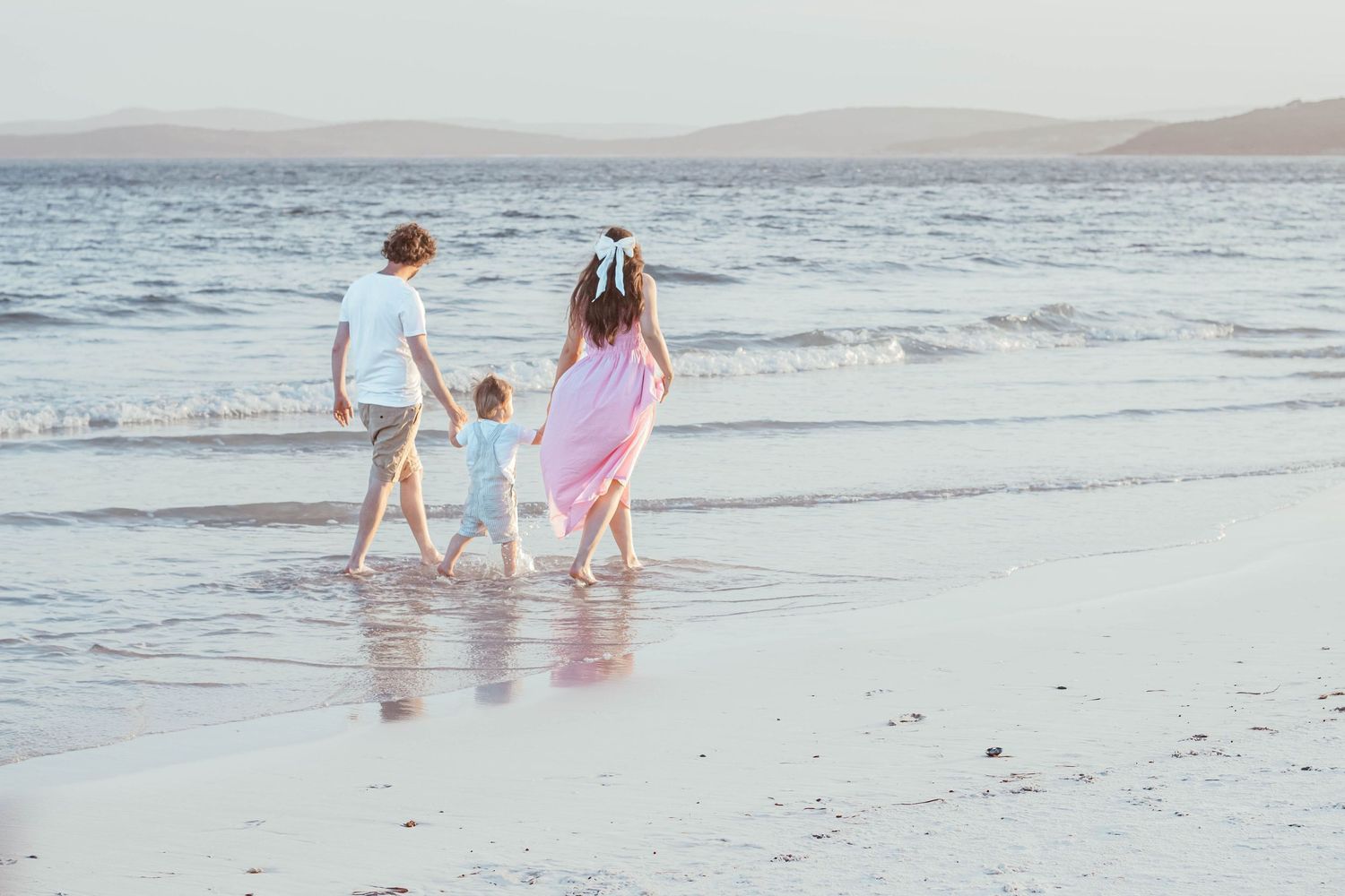 People walking together in matching pink and white outfits along a tranquil beach at sunset.