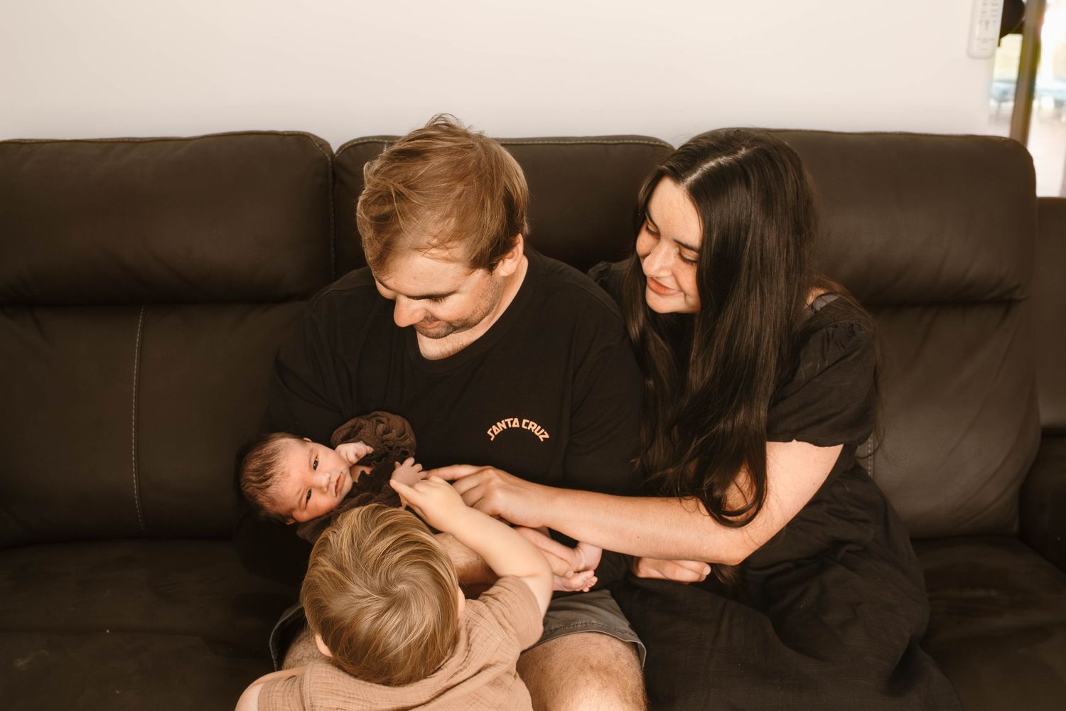 Family of three sharing tender moment while sitting together on brown leather sofa.