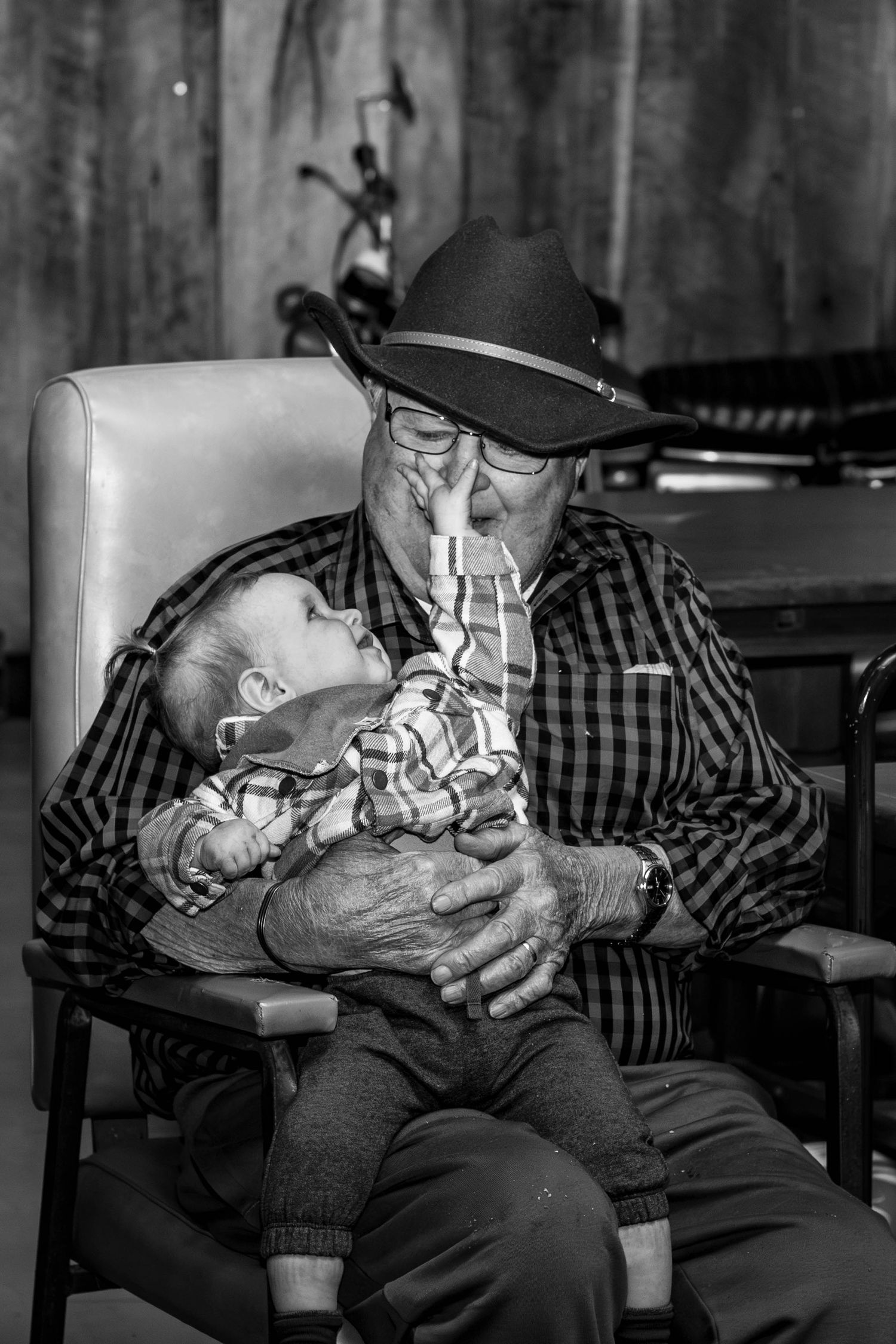 Black and white photo showing tender moment in leather armchair with rustic wood background.