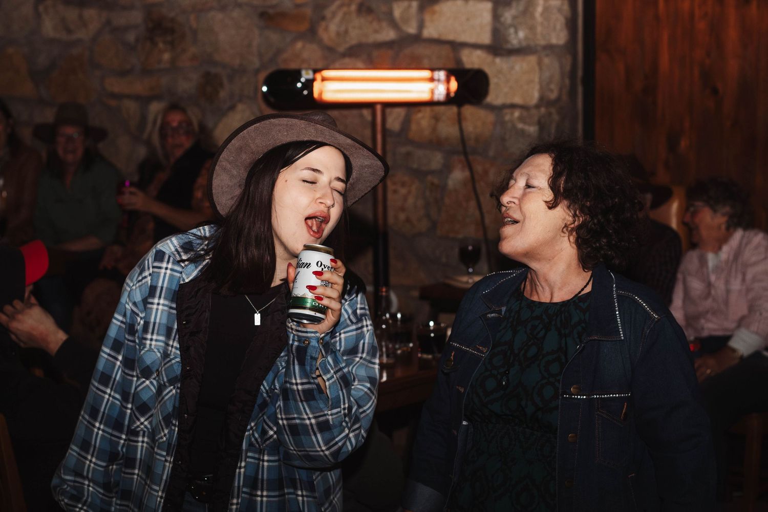 Two friends sharing laughs and drinks at a cozy bar with stone walls and warm lighting.