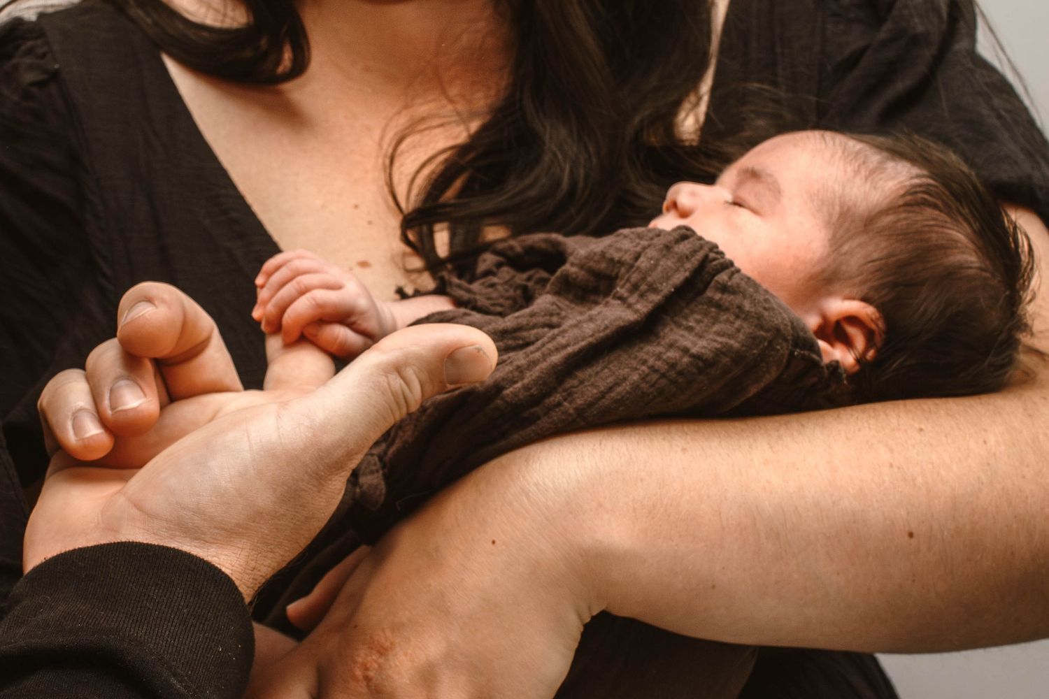 Intimate close-up of parents' hands gently touching their baby in warm tones.