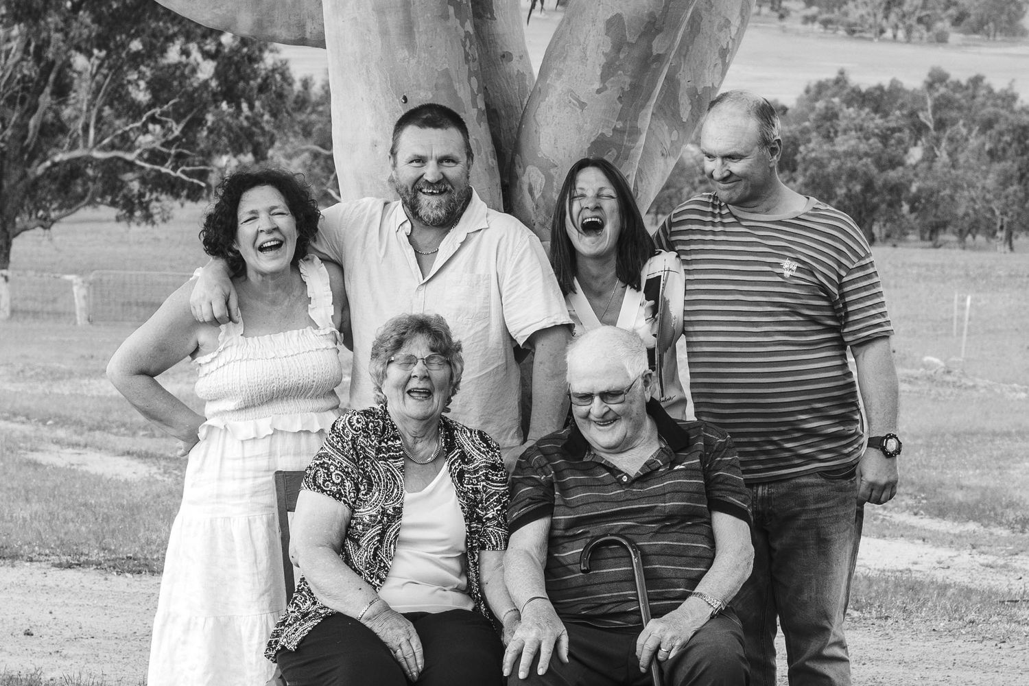 Black and white family portrait of multiple generations laughing together under a tree.