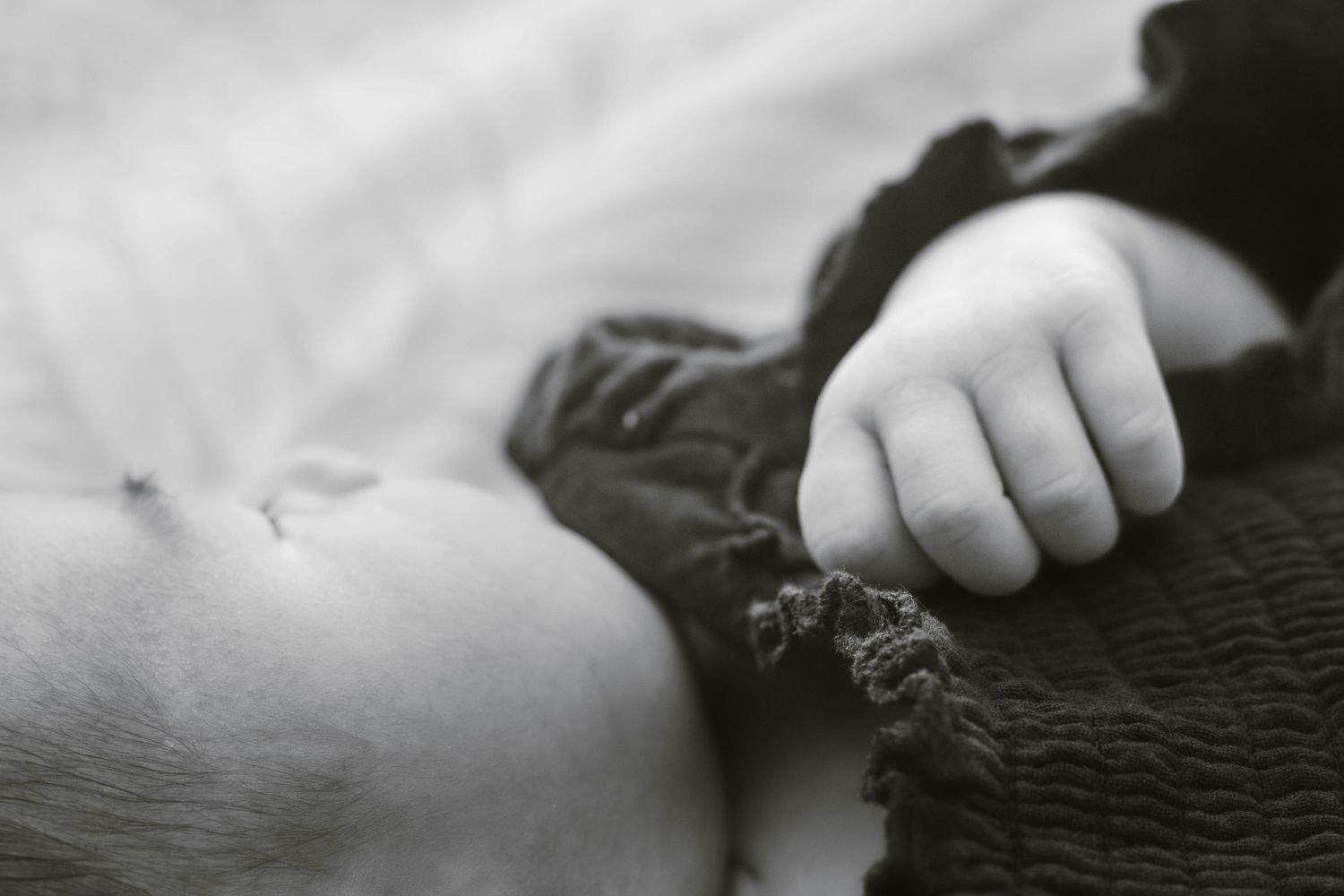 Black and white artistic portrait of a sleeping baby in textured clothing.