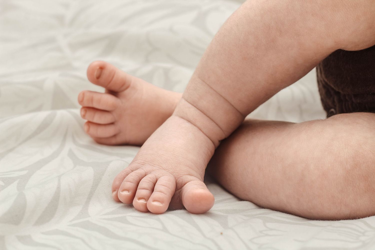 Tiny bare feet and legs of infant against white cotton sheets.