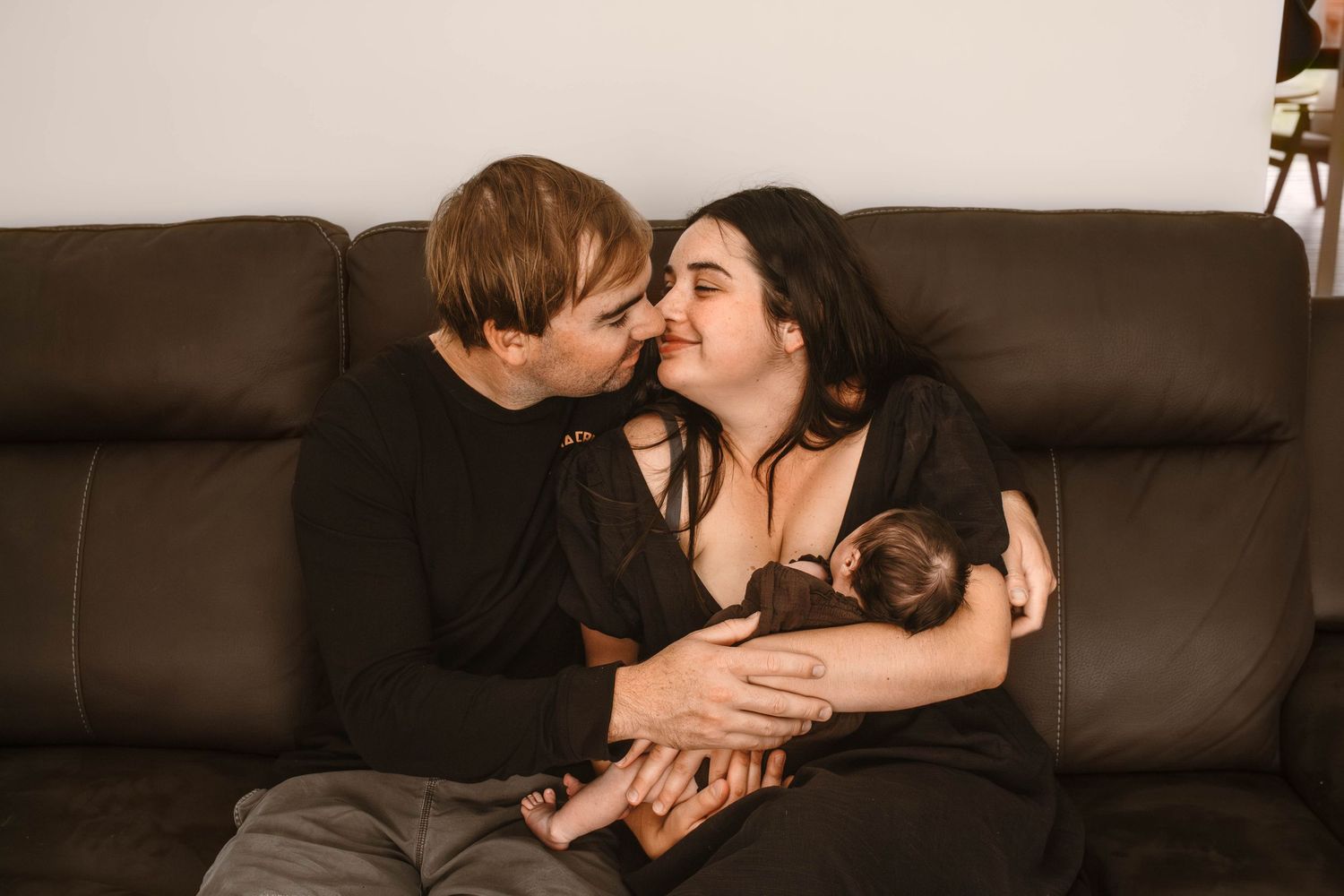 Intimate family moment captured on leather couch with newborn baby.