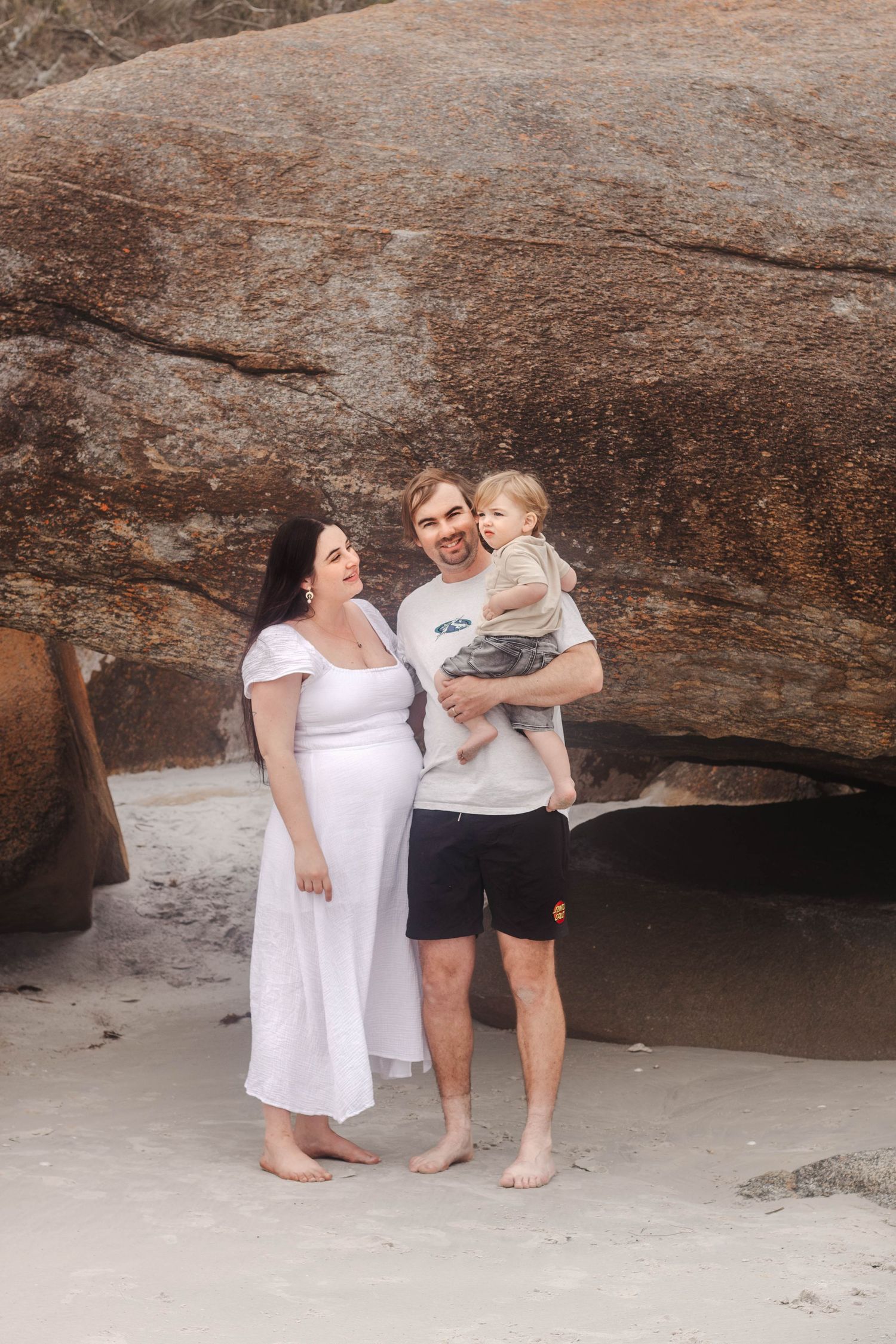 Family standing together on beach under large rock formation.