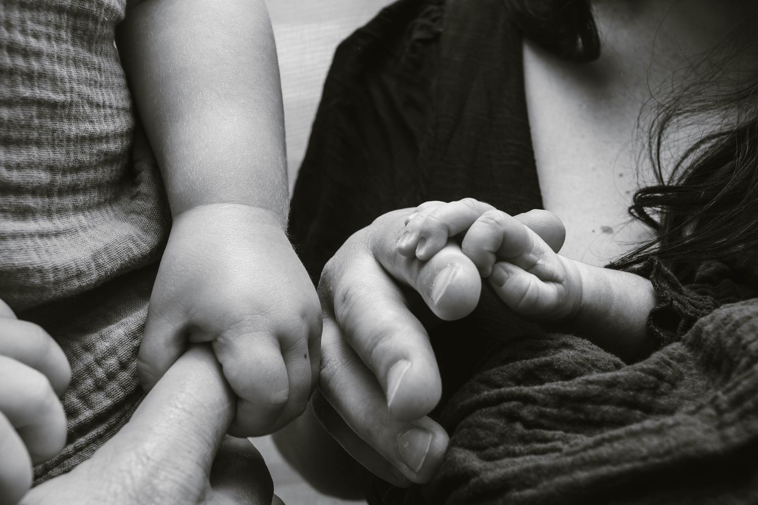 Black and white close-up of small hands intertwined in an intimate family moment.