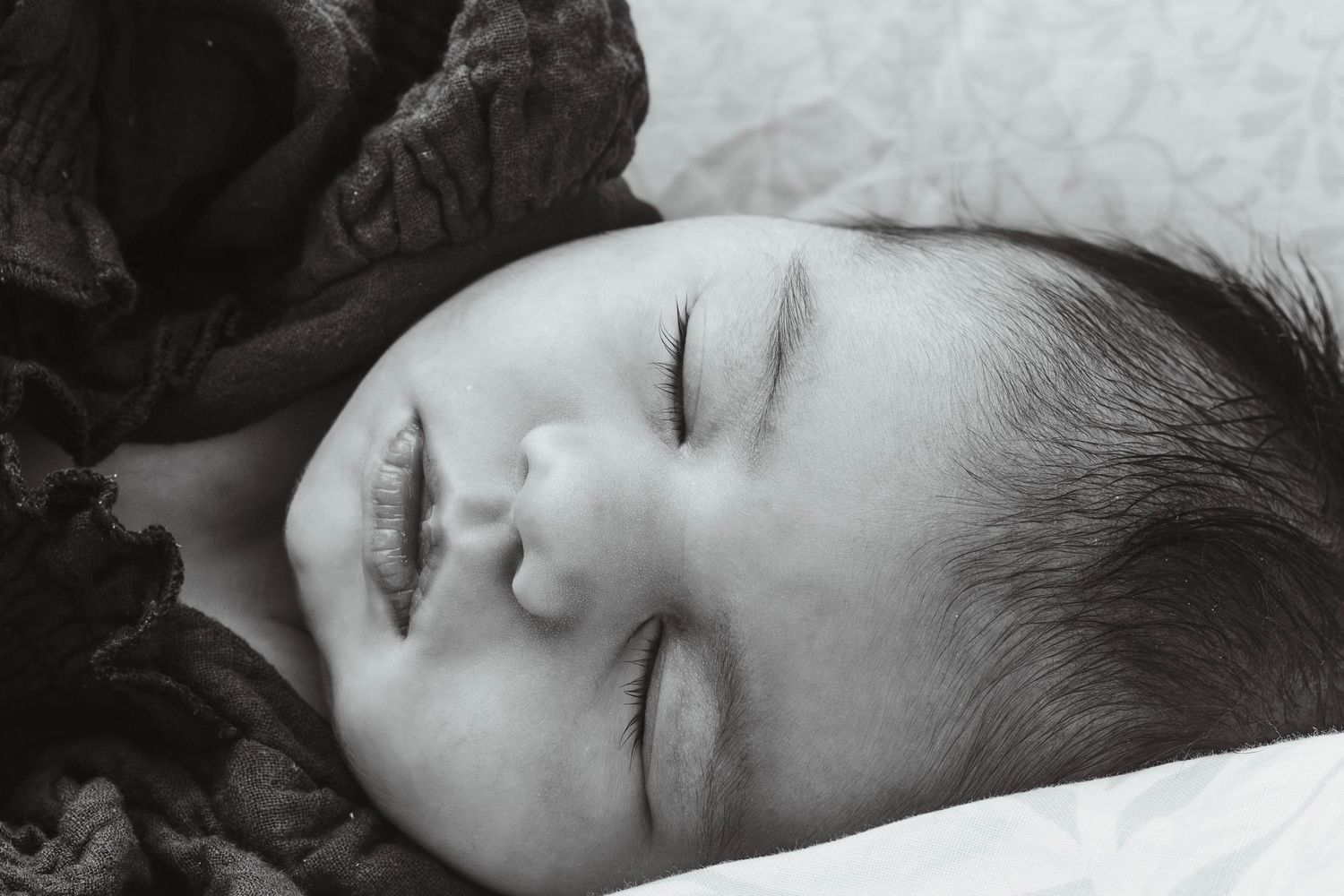 Close-up of peaceful sleeping baby with dark brown clothing against white bedding.