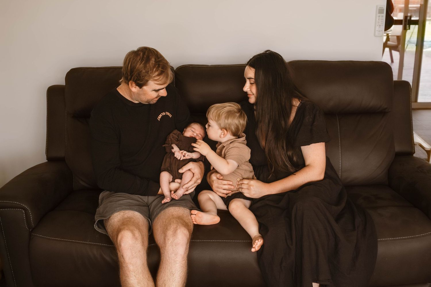 Happy family moment on a dark leather couch with warm lighting.