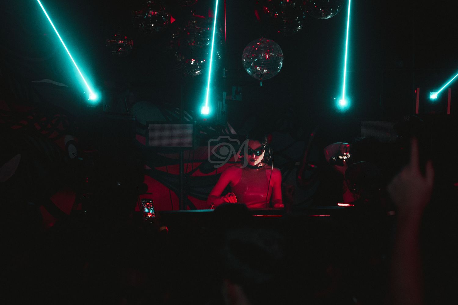 DJ booth illuminated by teal laser lights in a dark nightclub setting.