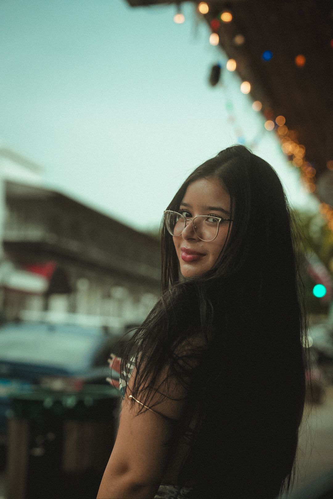 Portrait outdoors at dusk with string lights in background creating bokeh effect and shallow depth of field.
