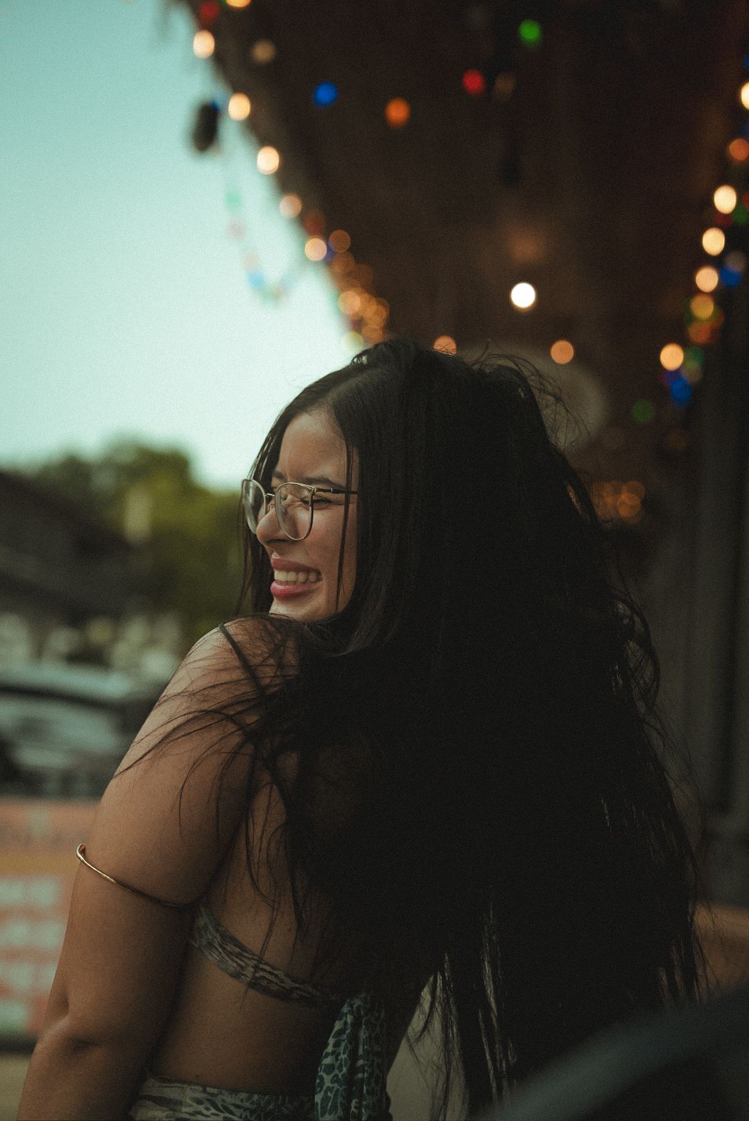 A candid side profile portrait of a person smiling and looking off-camera with blurred lights in the background.