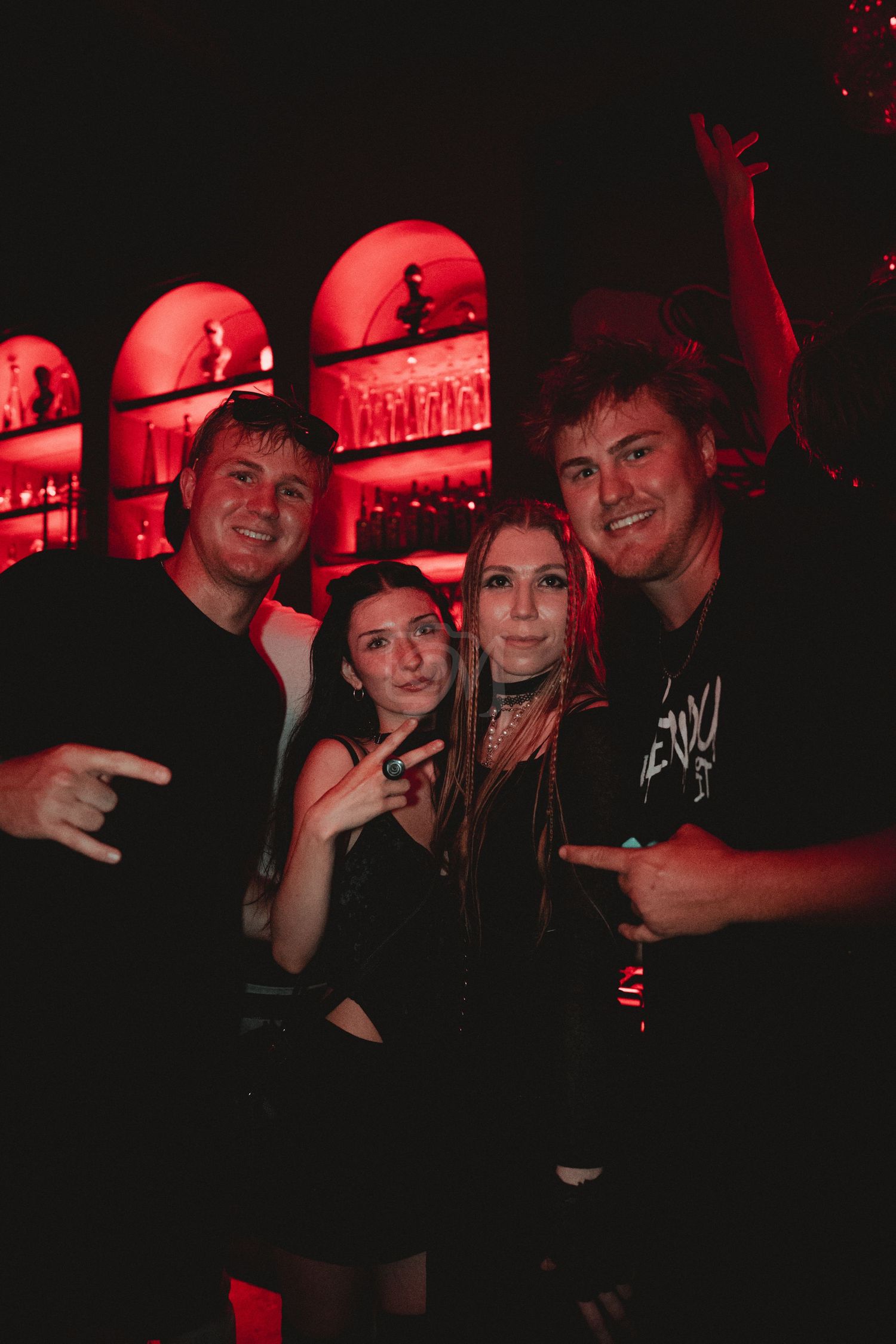 Friends posing together at a nightclub under red ambient lighting.