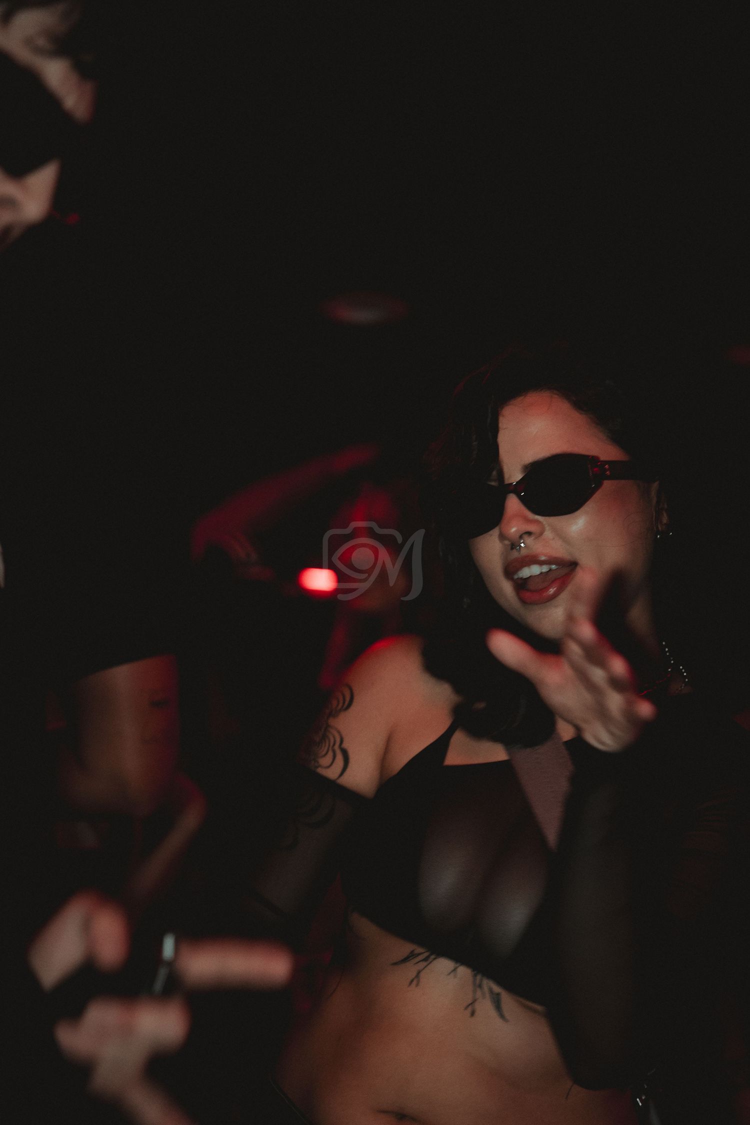 Energetic club performer in sunglasses dancing under red lighting.