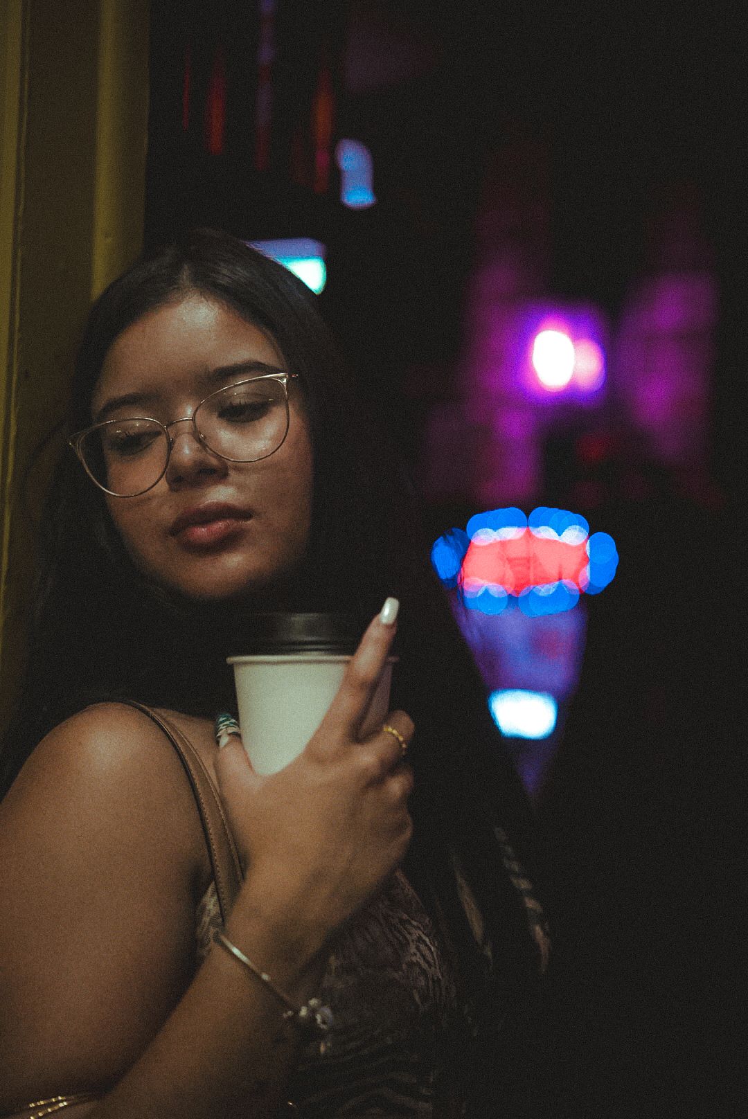 Glass of milk or cream being held with neon lights and dark atmospheric lighting in the background.