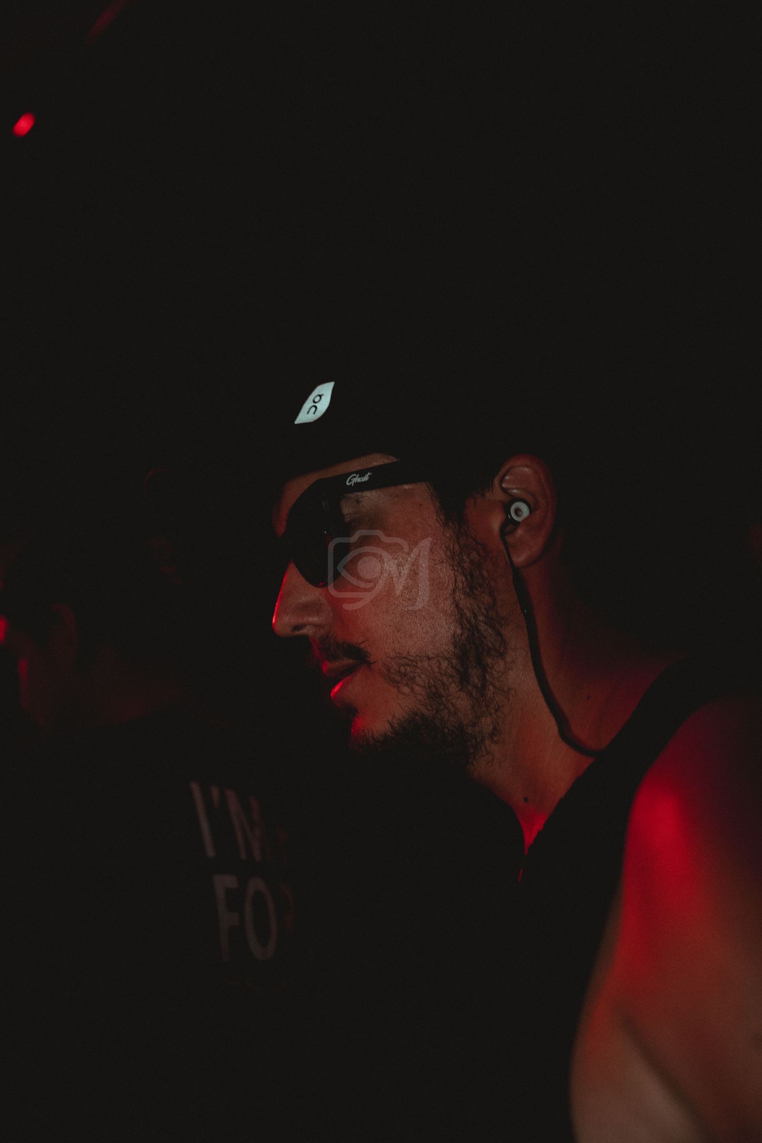 Side profile of someone wearing a cap and earbuds in dark red lighting.
