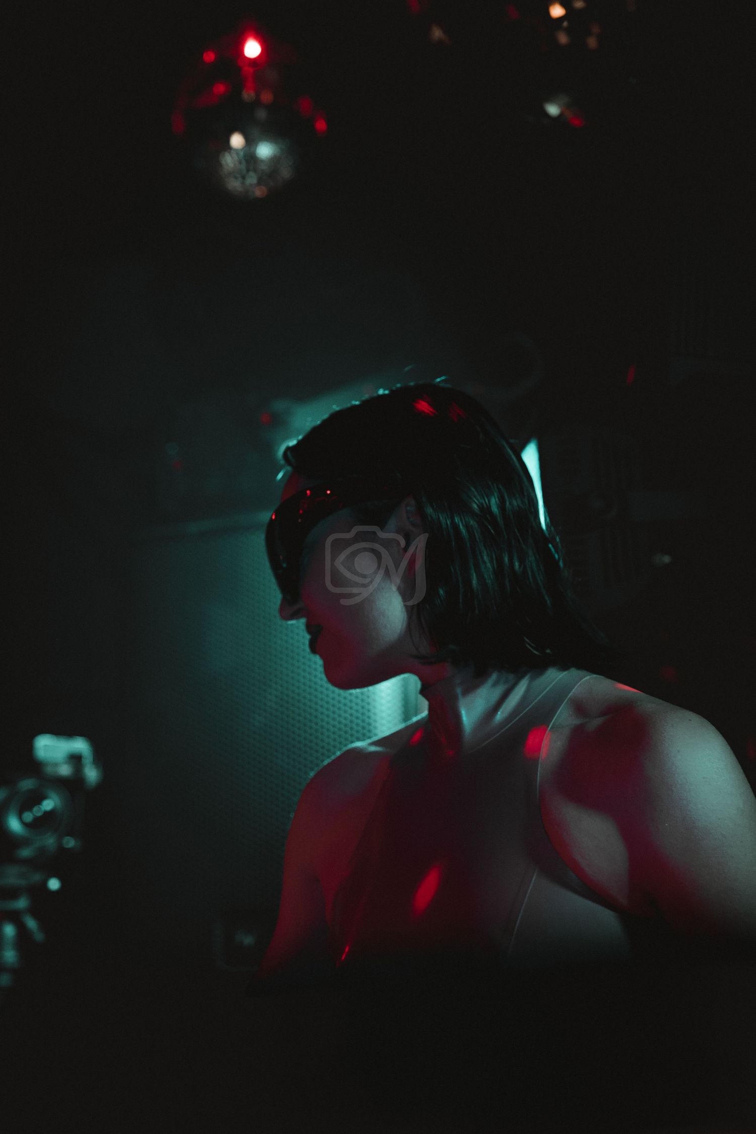 Silhouette of performer illuminated by red and teal lighting with disco balls overhead.