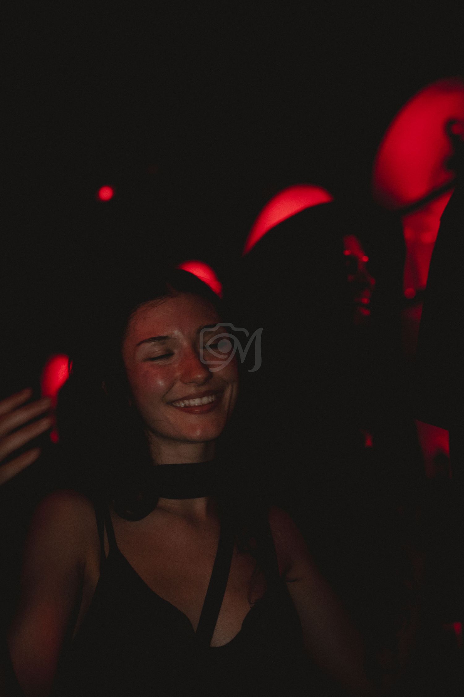 A dimly lit nightclub scene with red lighting and someone dancing in the shadows.