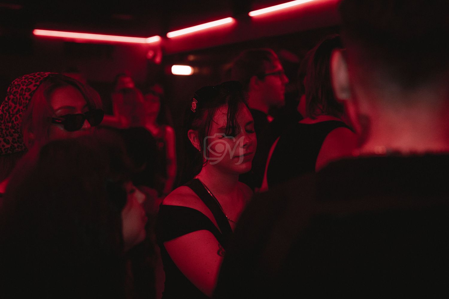 Crowded nightclub scene with people dancing under red neon lights.