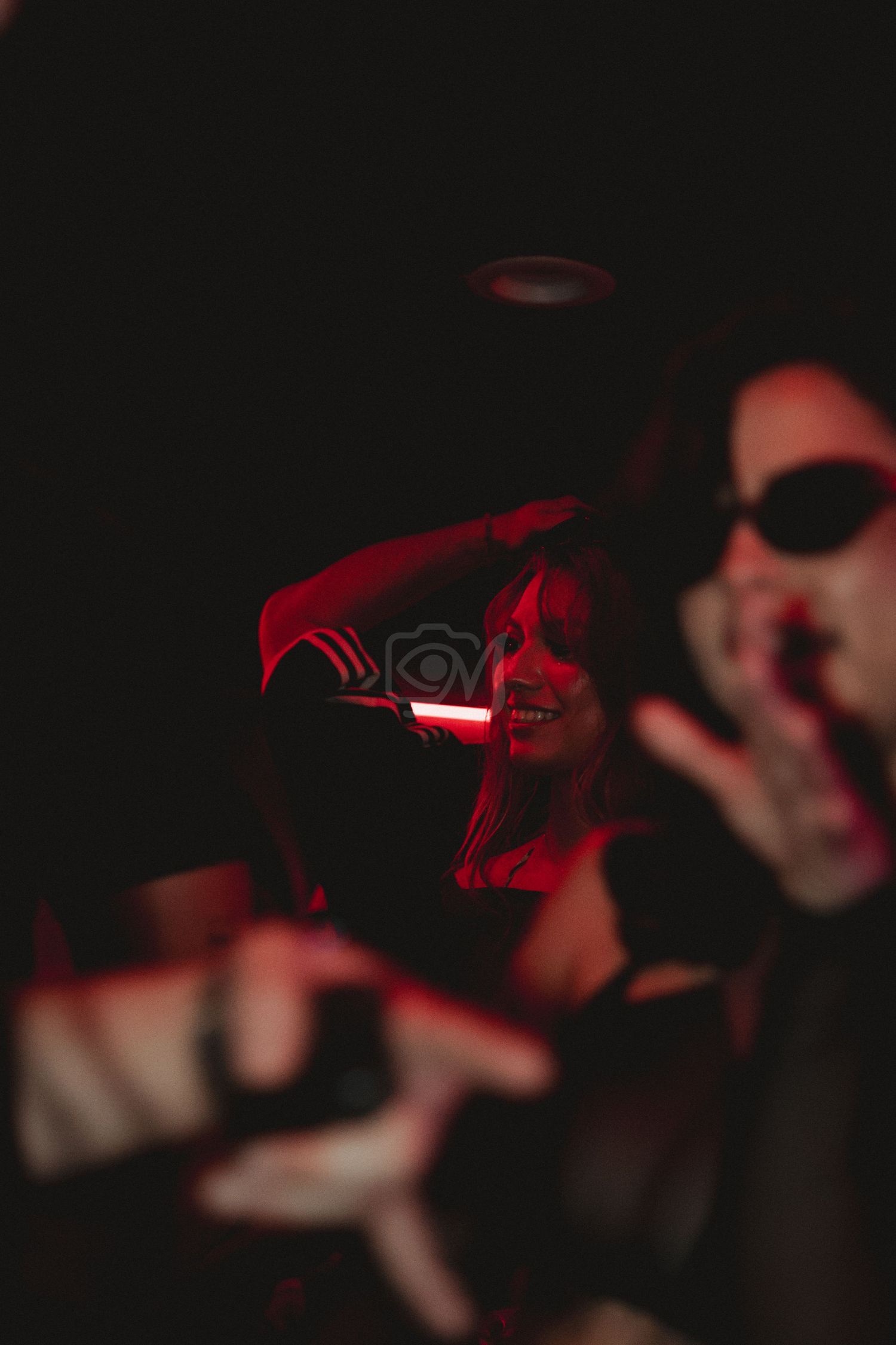 Artistic nightclub photo with red lighting and sunglasses in soft focus.