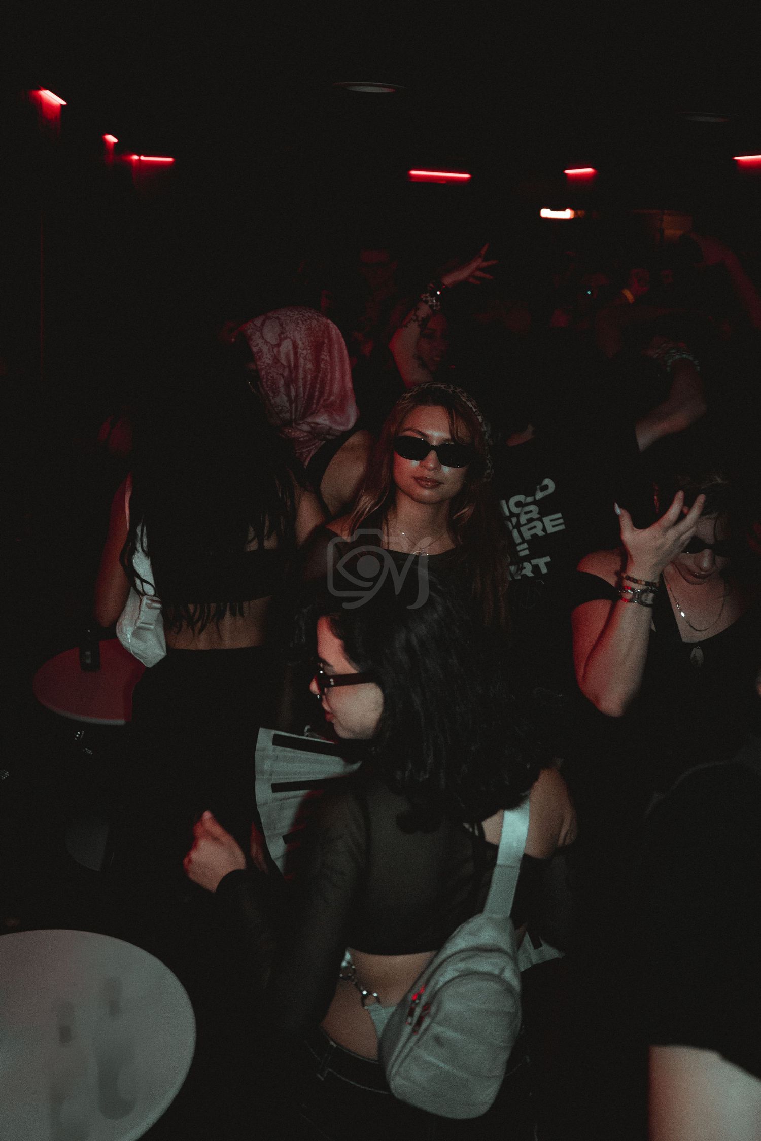 People dancing and partying in a dark nightclub with red lighting and neon accents.