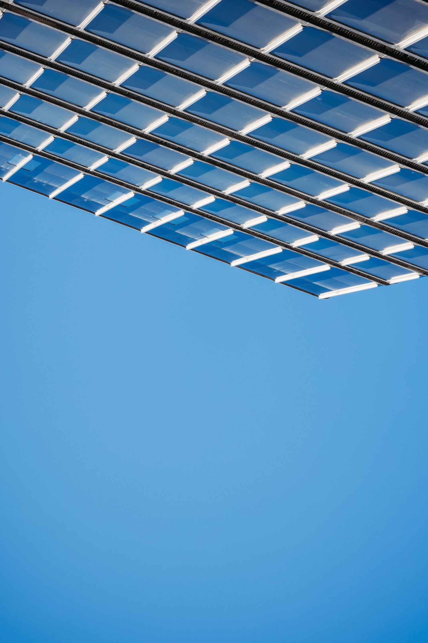 Modern glass building facade with geometric grid pattern against a clear blue sky, showcasing contemporary architecture design.