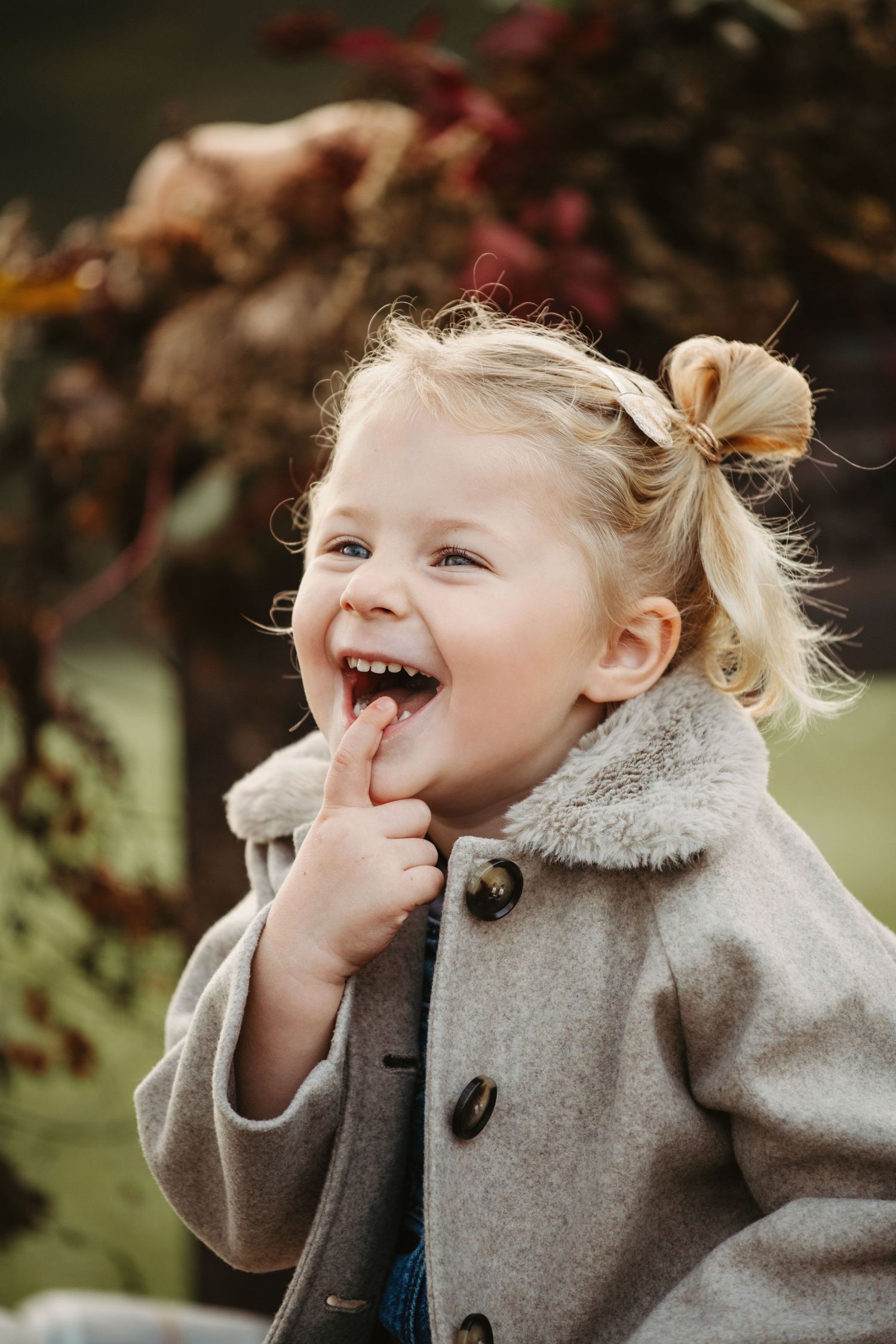 A sequence of photos showing a child in a grey coat laughing and playing outdoors with autumn foliage in the background.