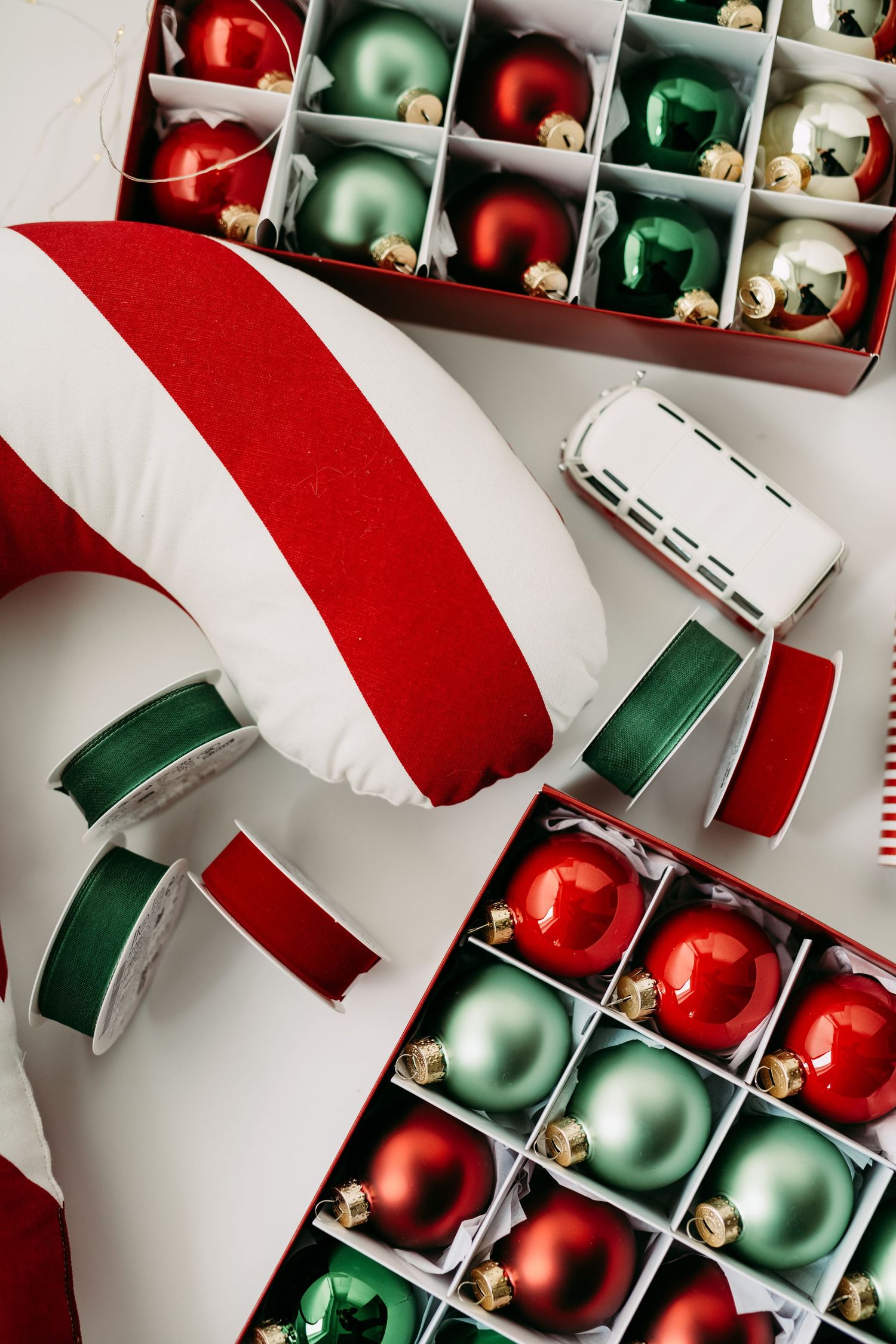 Red and green Christmas ornaments arranged in box with striped holiday decor.
