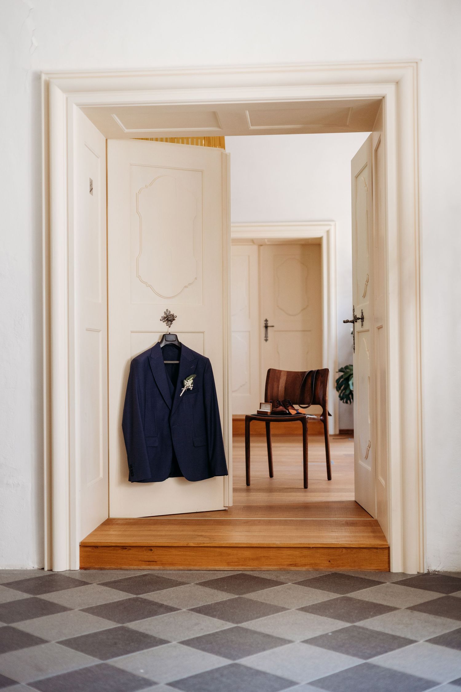 Navy blue blazer hangs in minimalist white interior room with geometric patterned tile floor and doorways.
