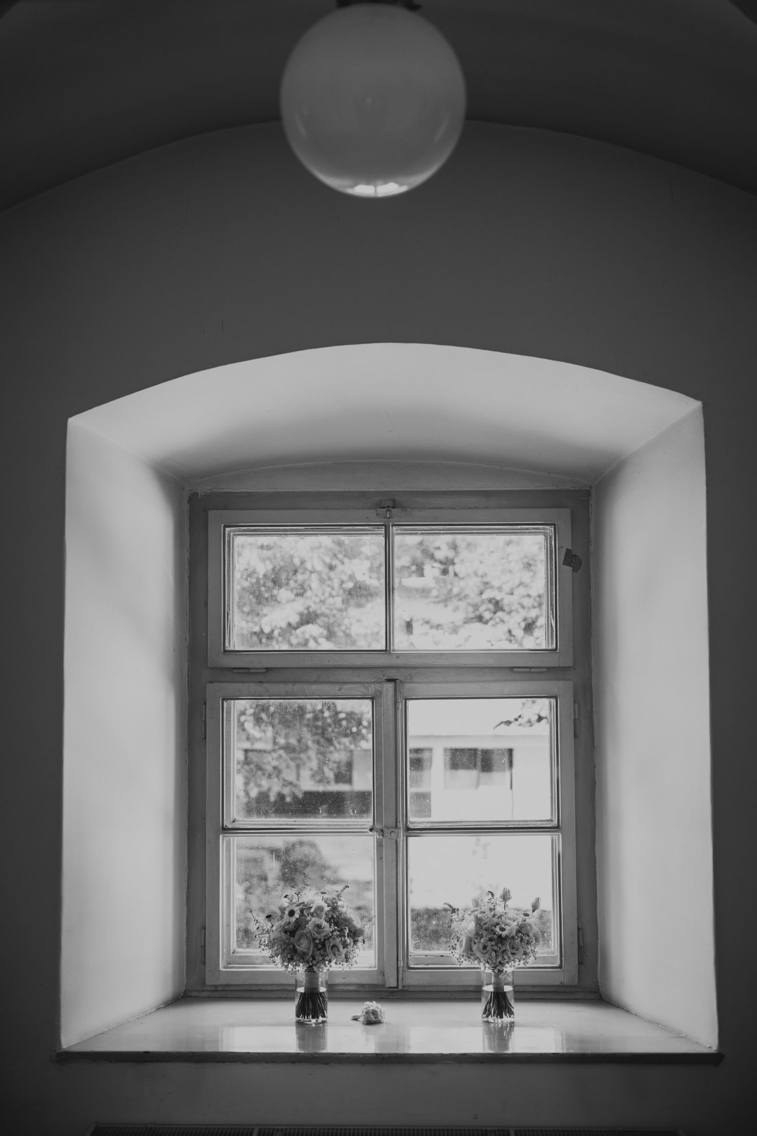 Black and white photograph of a window alcove with two small vases of flowers on the windowsill.