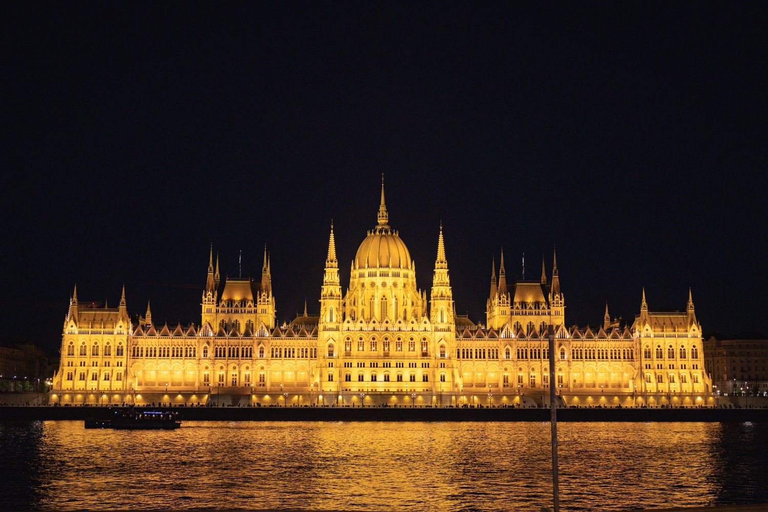 Historic Parliament Building of Budapest lit up at night with its reflection shimmering on the water.
