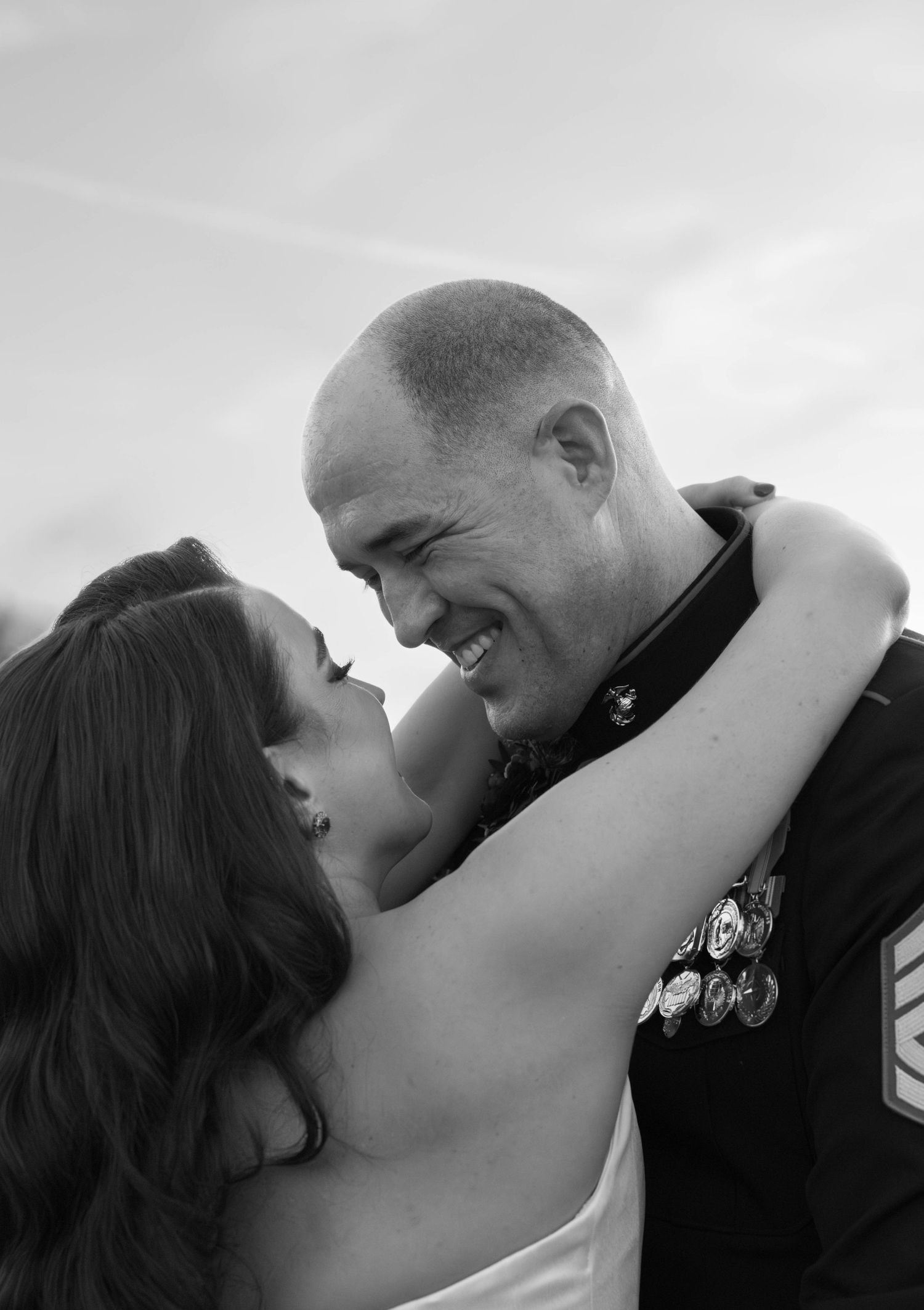 Black and white photo of a smiling military man in uniform embracing a woman, sharing a romantic moment outdoors.