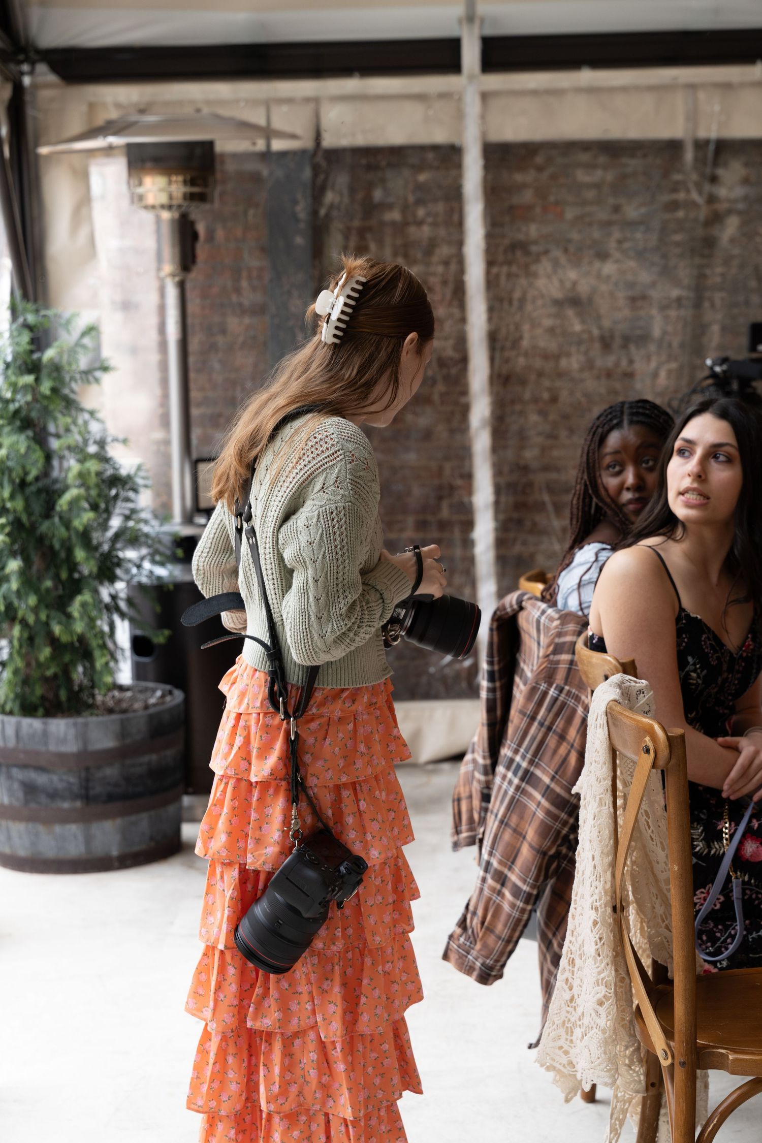 Three stylish women in bohemian outfits browse clothing at an outdoor fashion market.