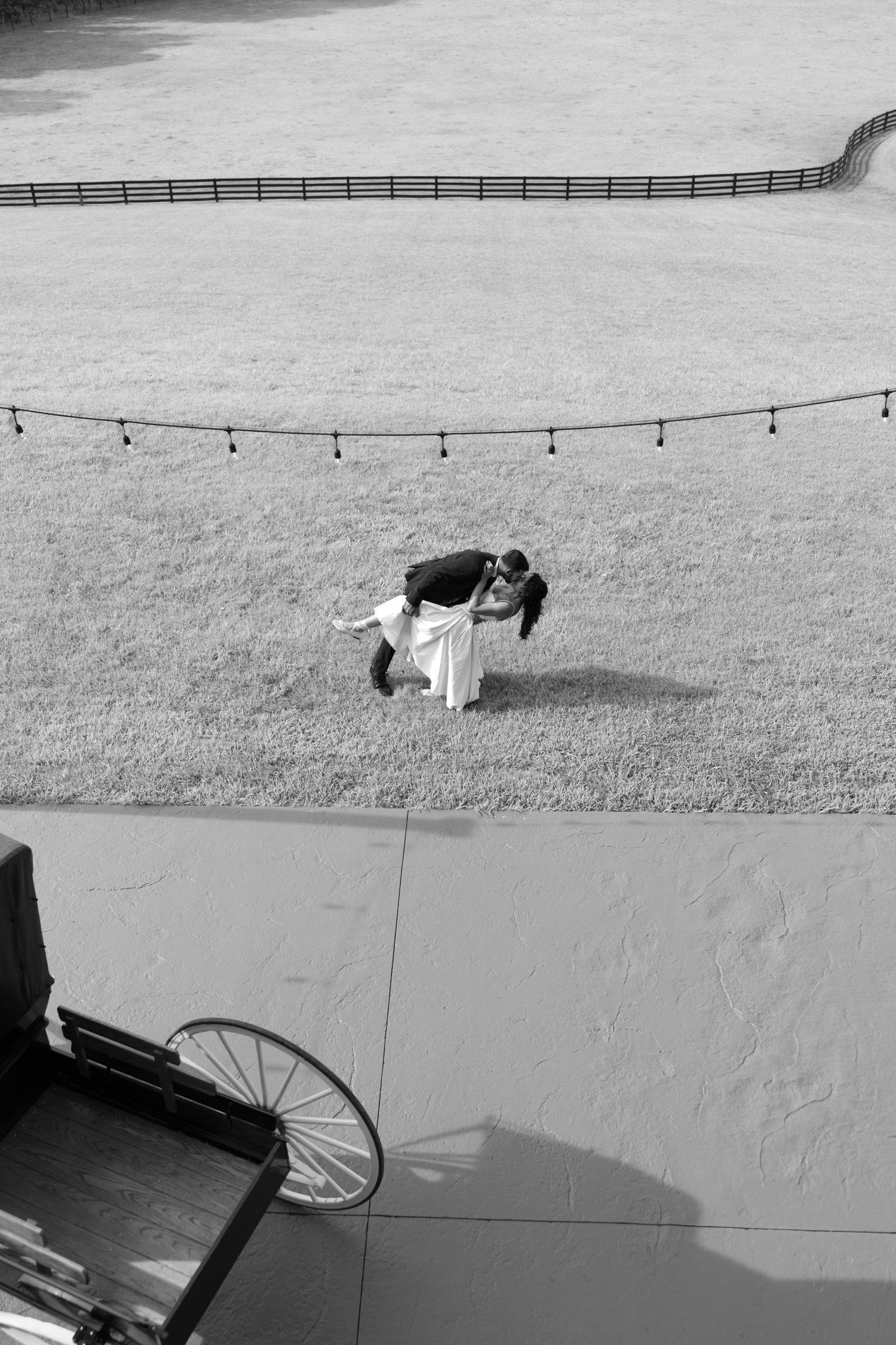 A black and white aerial view shows people lying on a concrete surface casting dramatic shadows on the ground.
