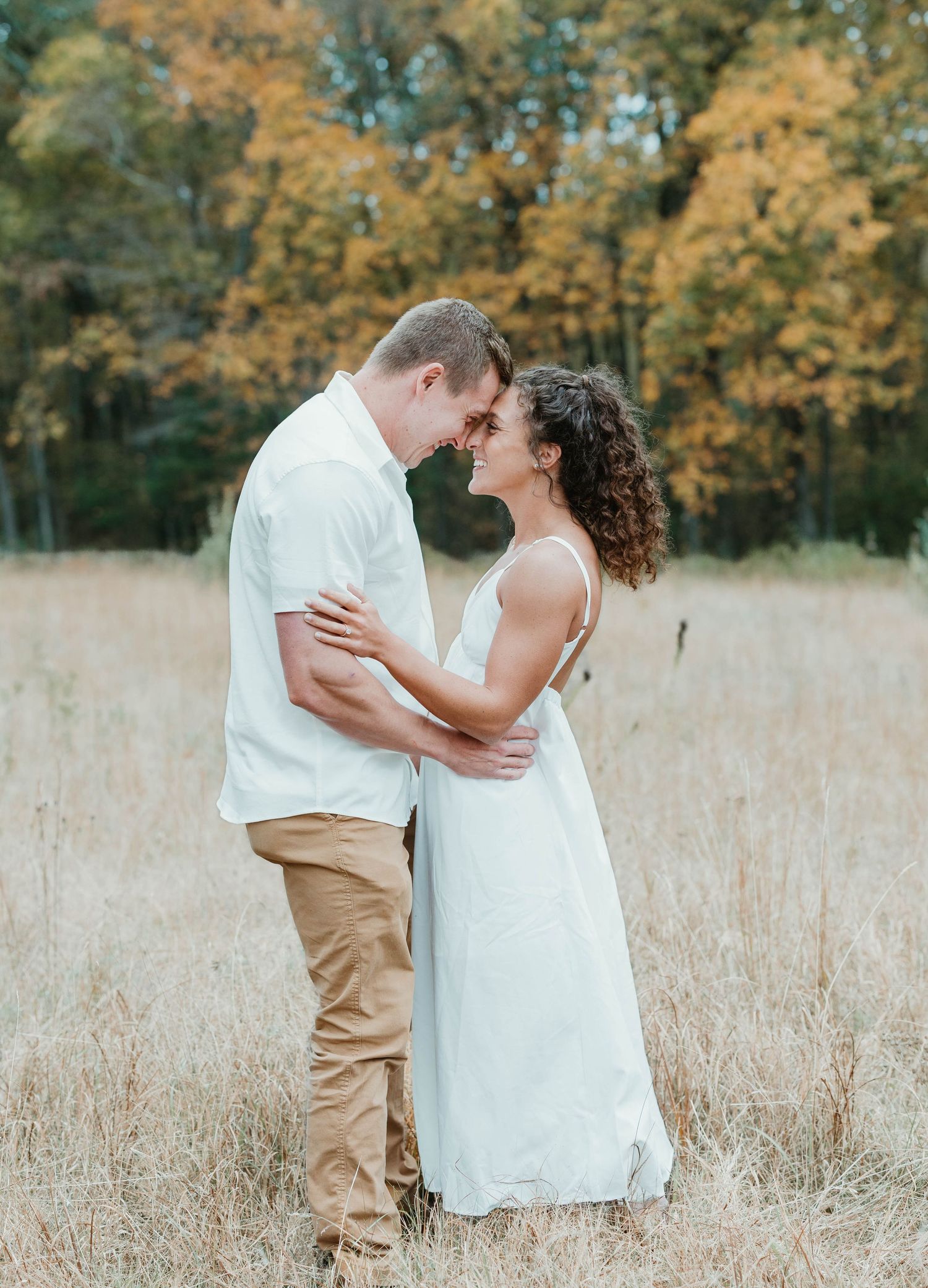 A couple shares intimate moments in a golden autumn field wearing white and khaki outfits.