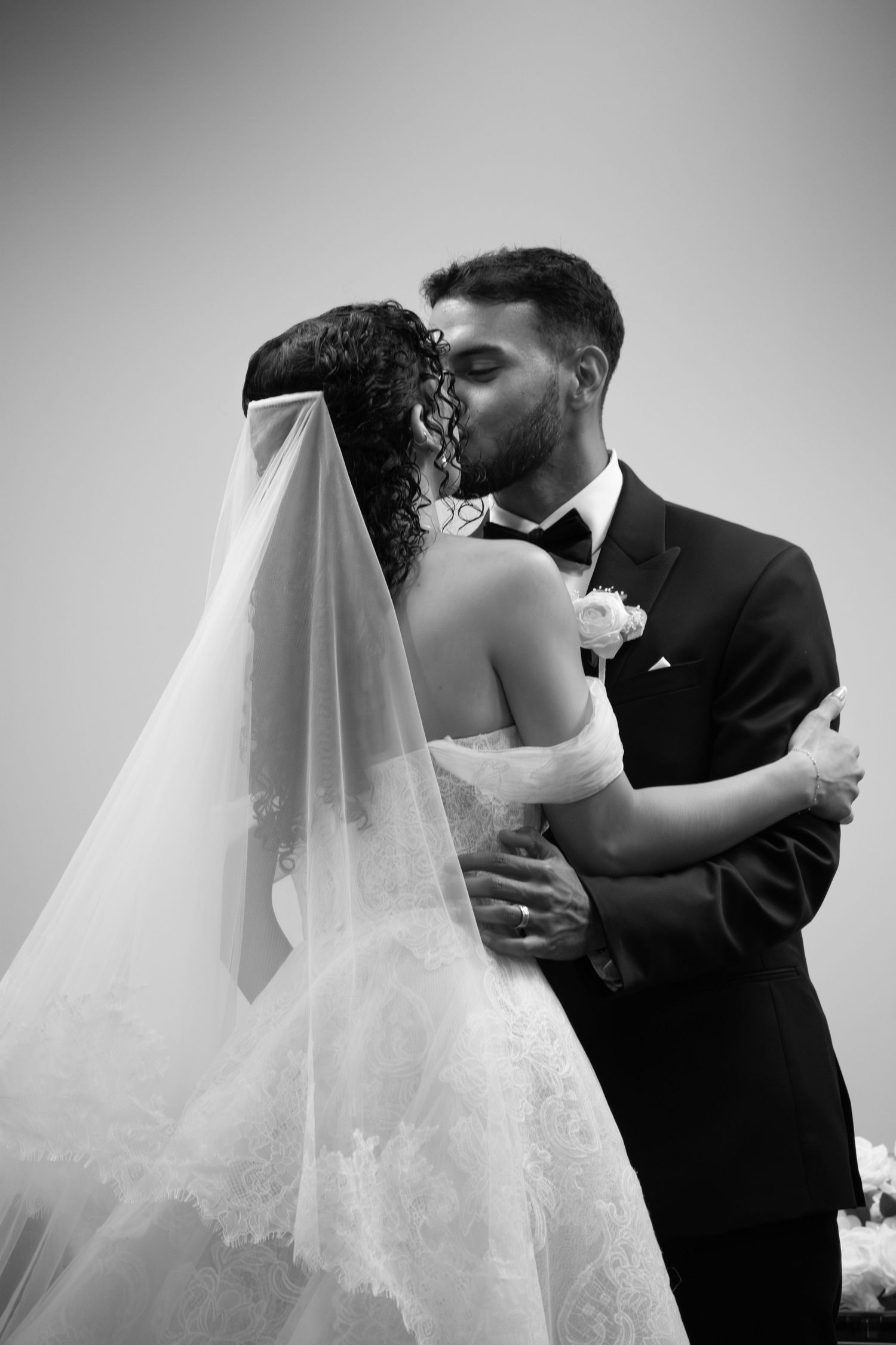 Black and white photo of bride and groom sharing a romantic first kiss at their wedding ceremony.