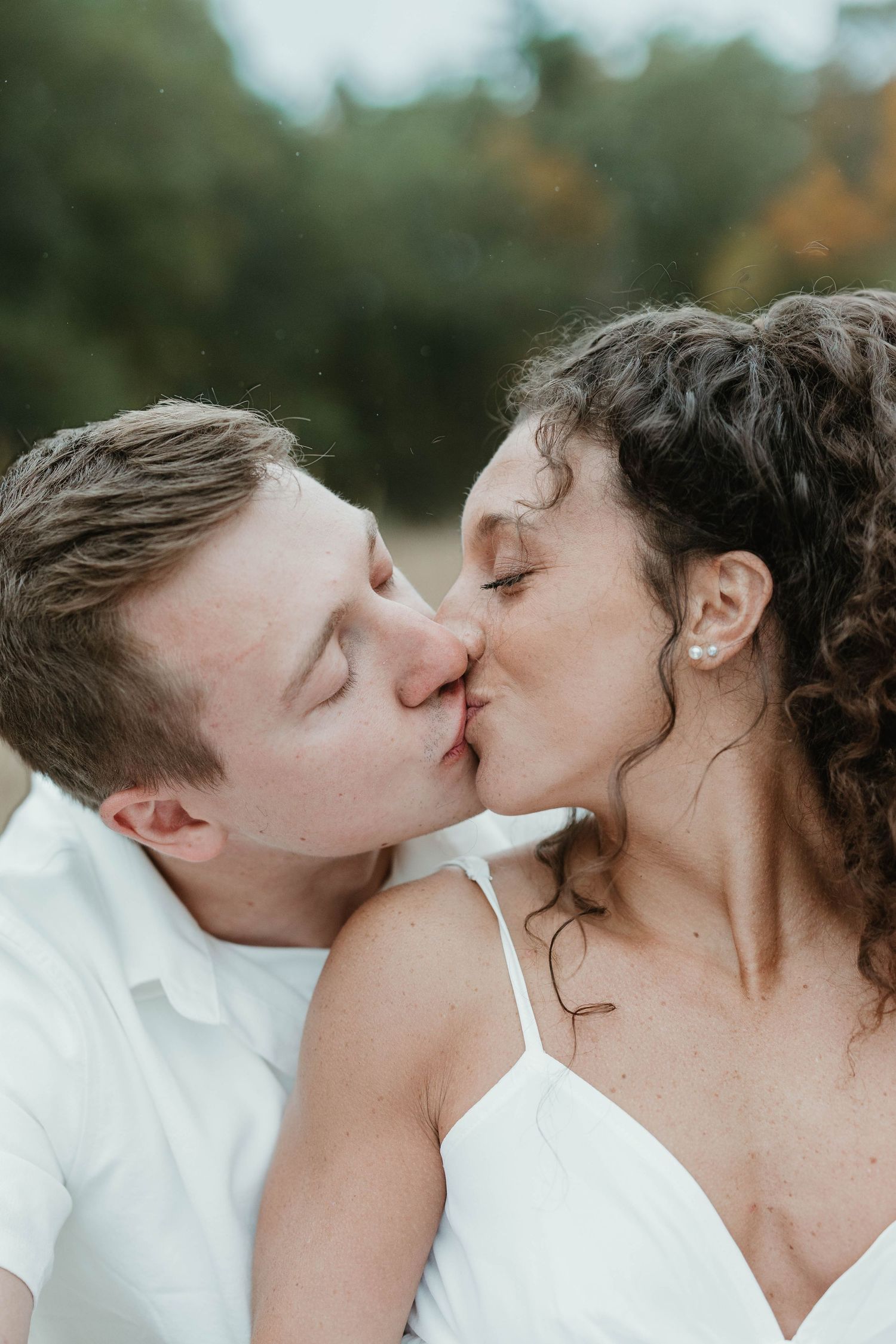A romantic sequence of close-up photos showing a tender kiss between a couple in white attire outdoors.