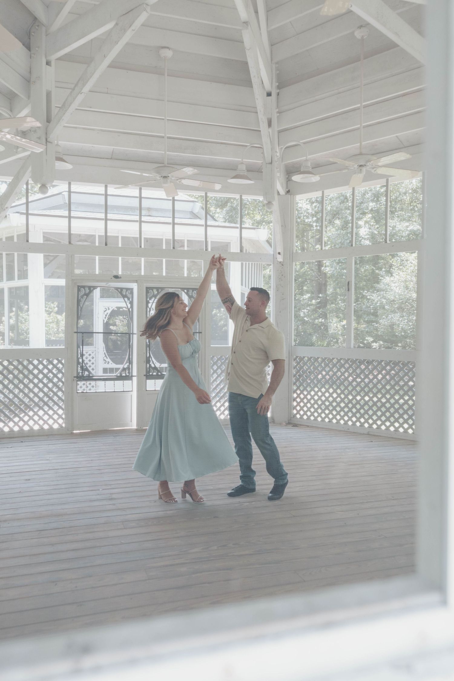 People dancing together in a bright white gazebo or covered pavilion with lattice railings and wooden flooring.