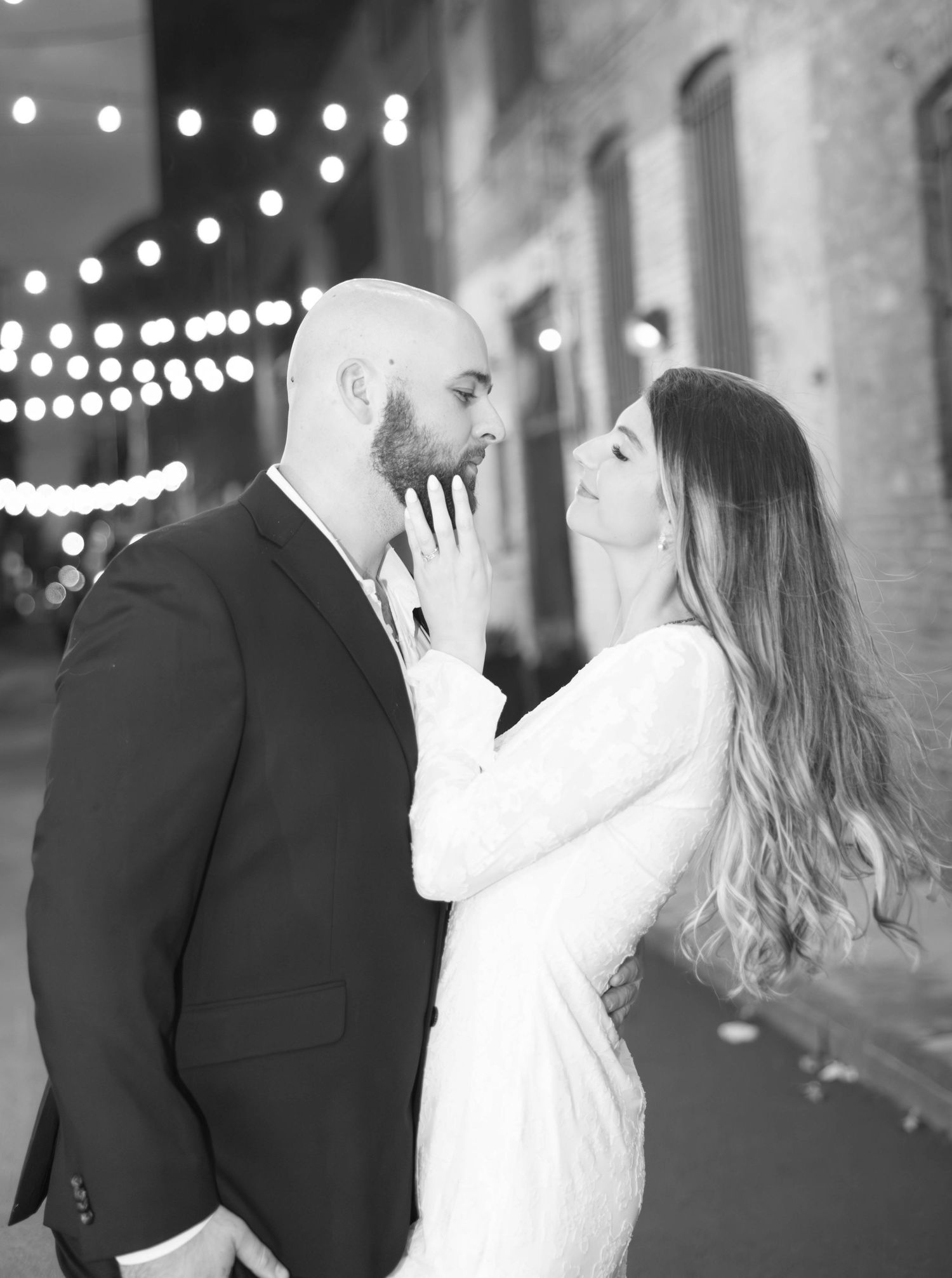 A romantic black and white photo series of a couple in formal attire sharing intimate moments under string lights.