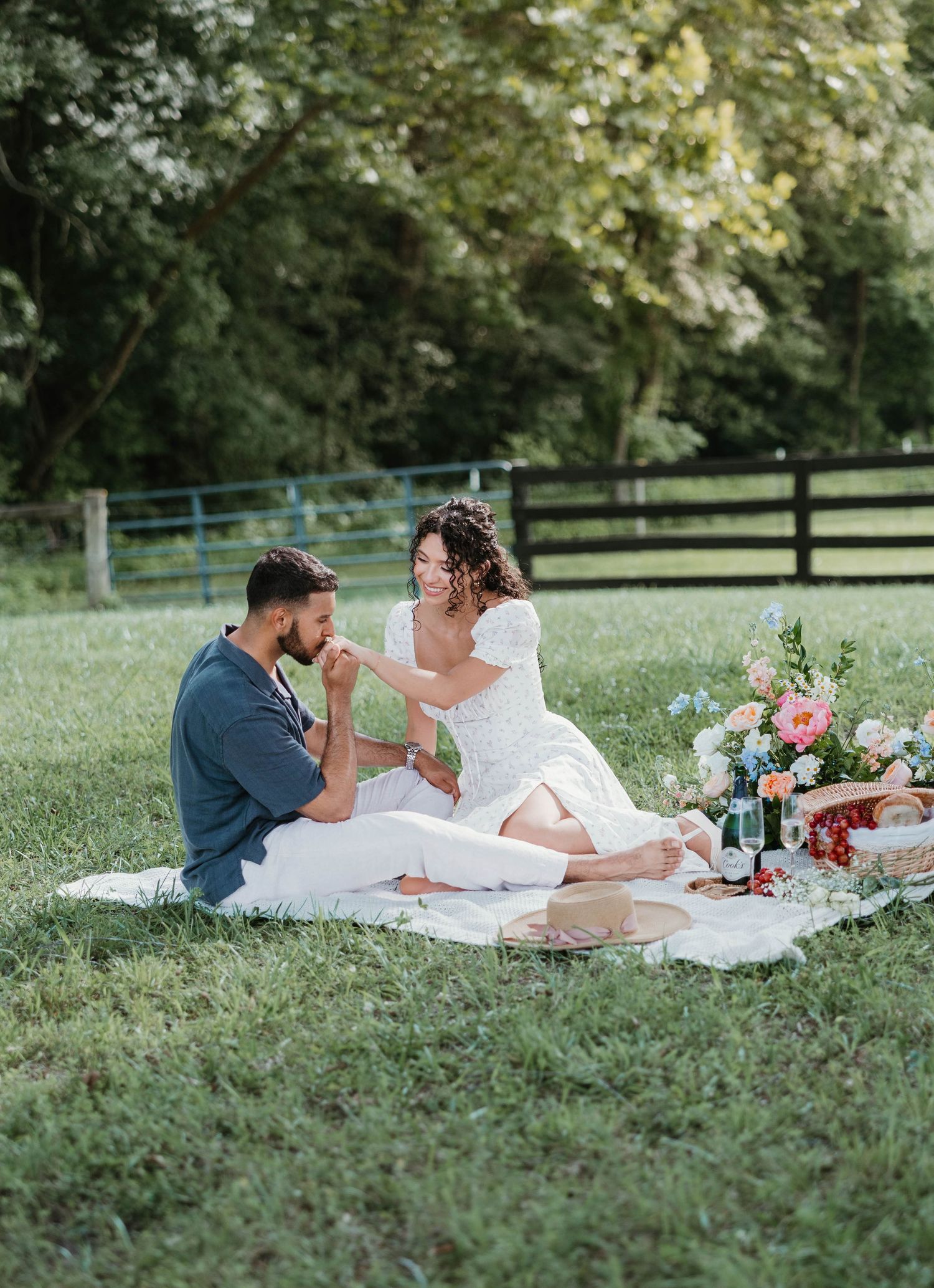 A couple enjoys a romantic picnic on a grassy lawn with wine and snacks on a sunny afternoon.